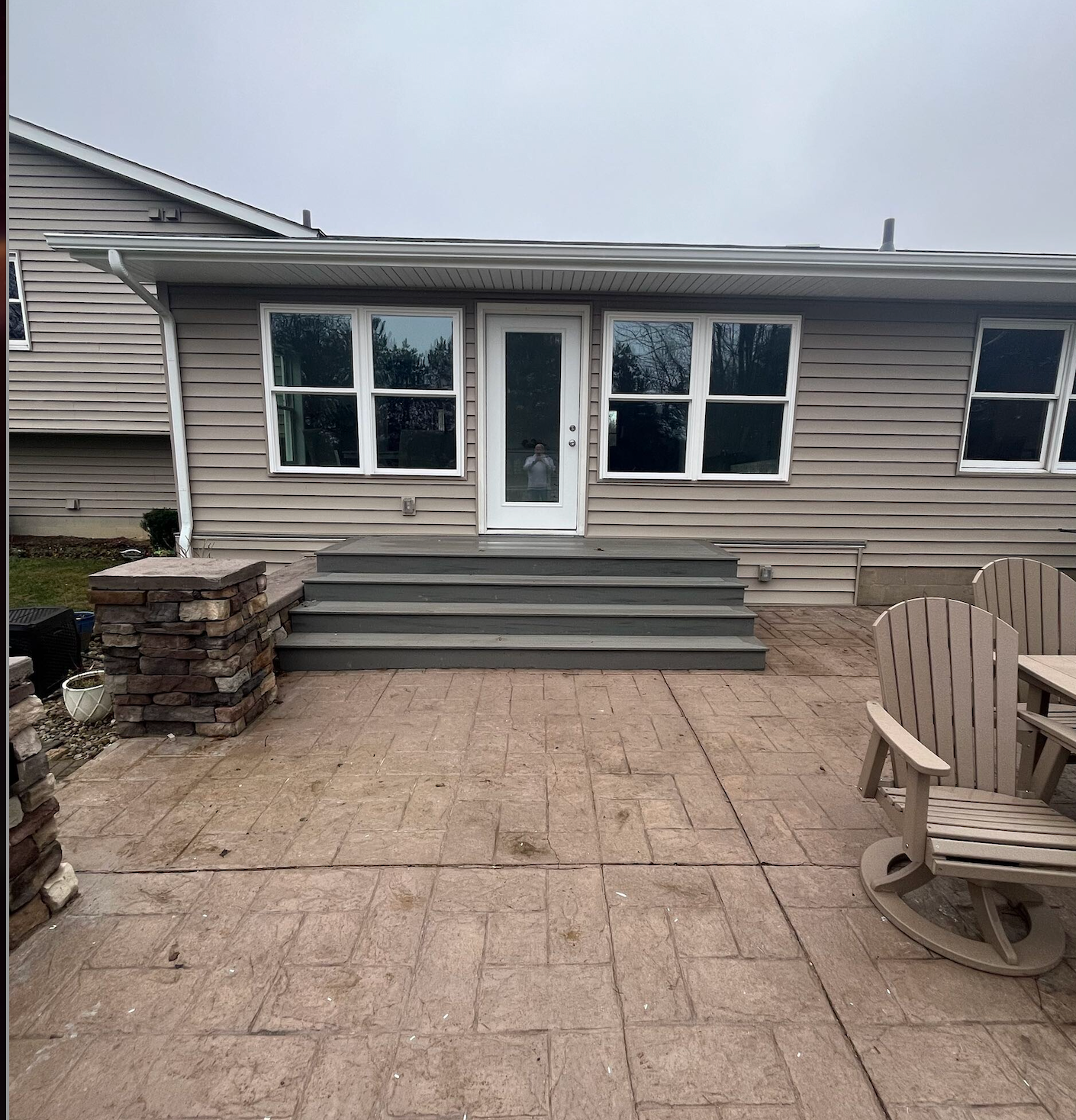 Backyard patio with steps leading to a beige house entrance and windows, with a chair and brick columns on the sides