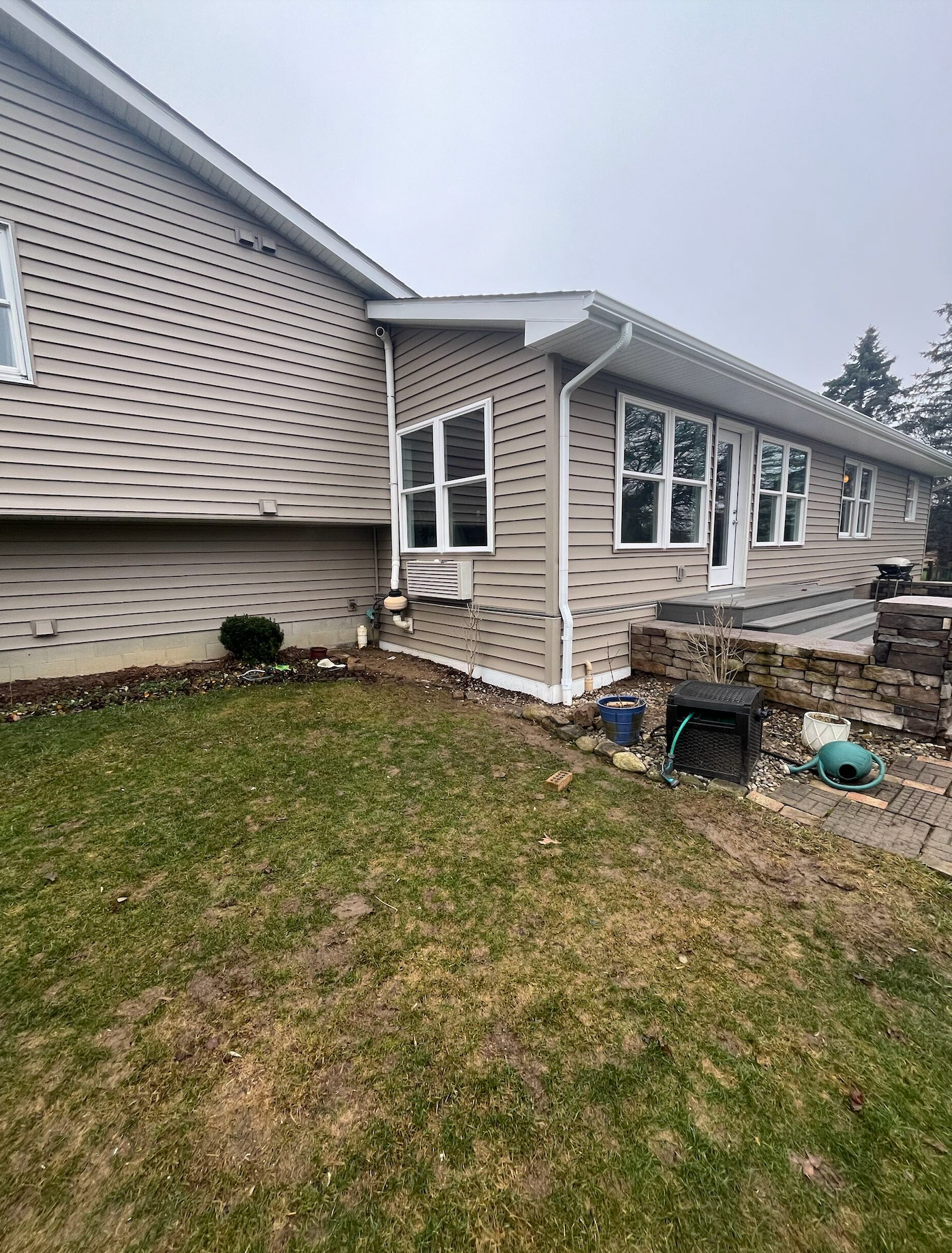 Suburban house exterior with beige siding, white windows, and a small patchy lawn on an overcast day