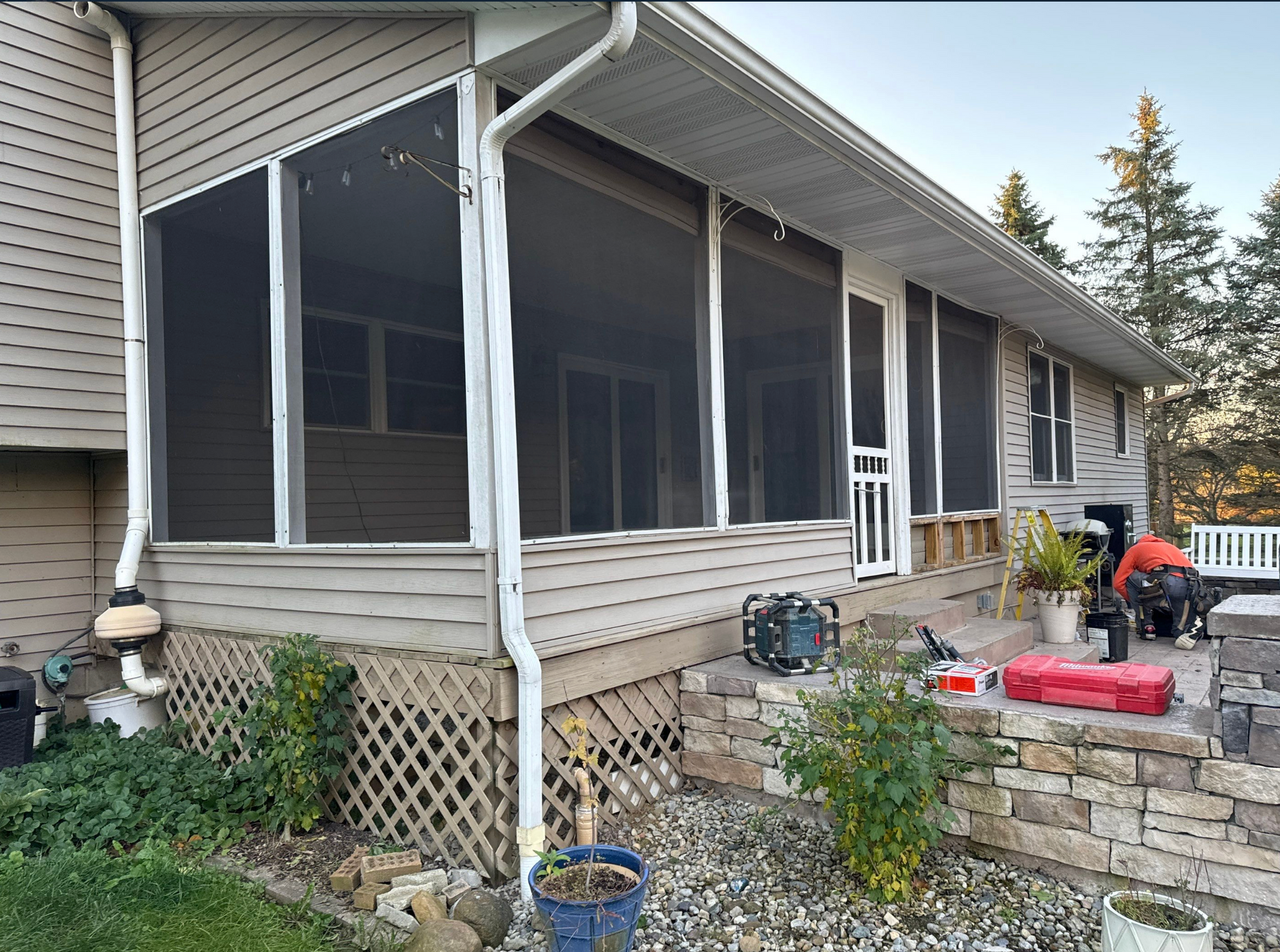 Screened porch with white siding, gardening tools, and a person tending items on the stone steps