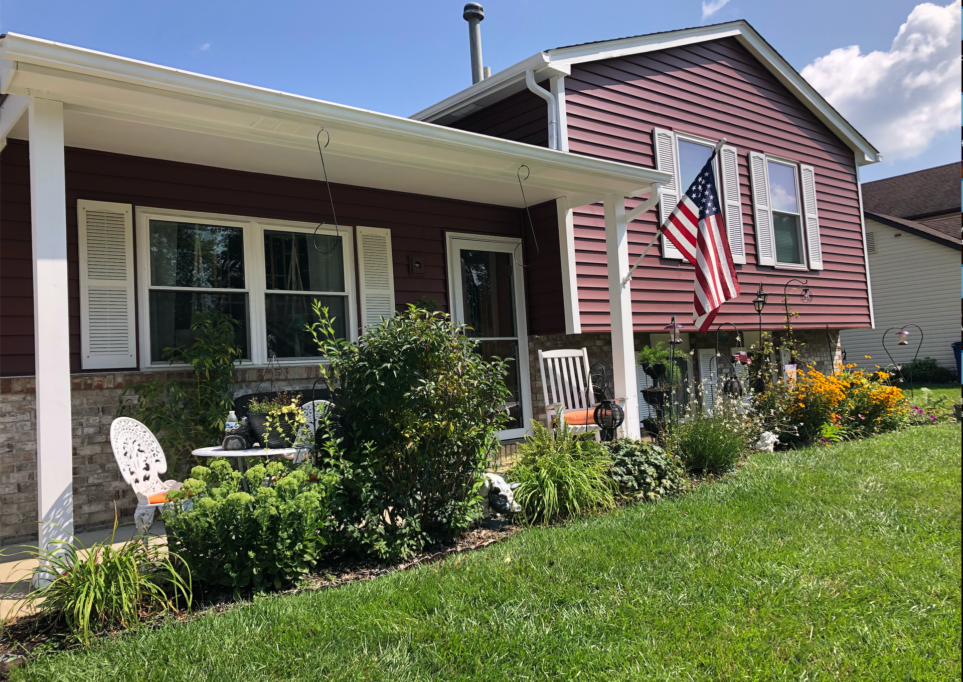 Suburban house with a front porch, American flag, and flowered lawn on a sunny day