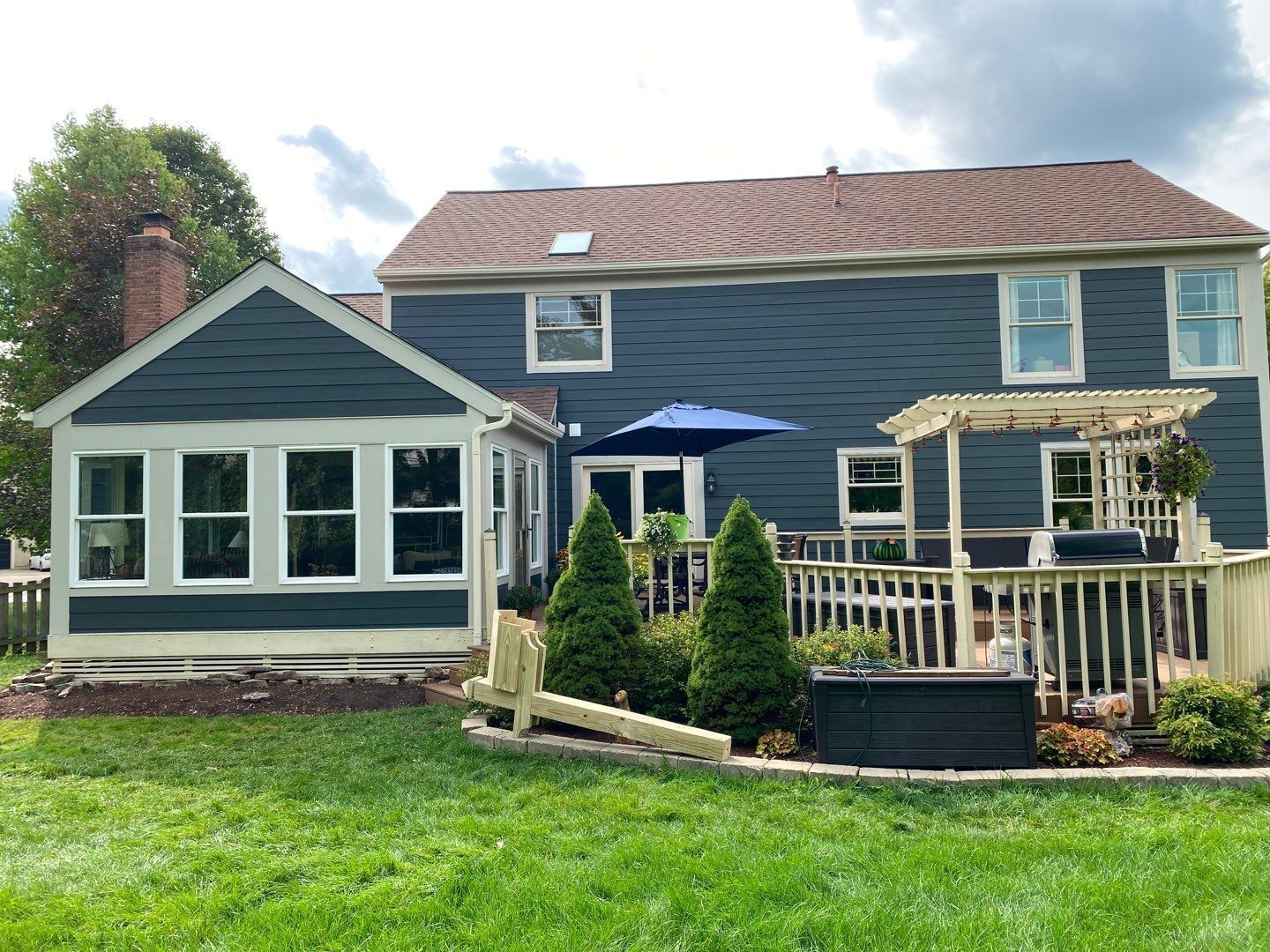 Blue two-story house with sunroom, deck, and patio furniture in a green backyard