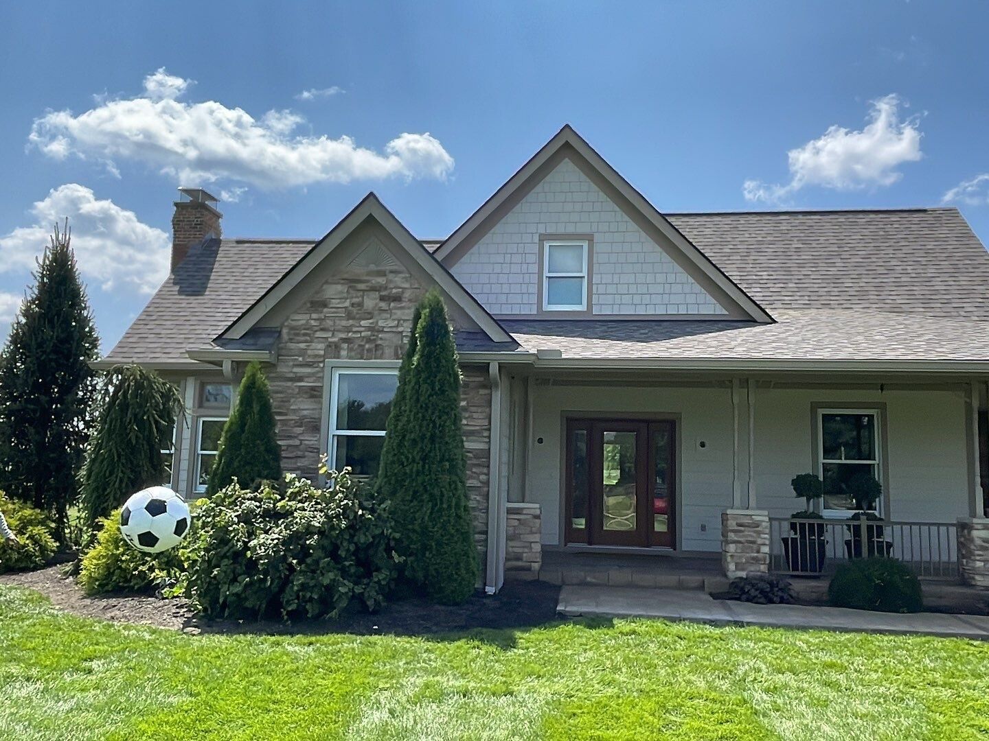 Suburban house with stone facade, front porch, manicured lawn, and a soccer ball in the yard