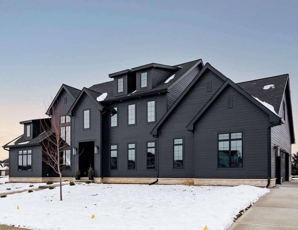 Modern dark-gray house with snow-covered yard and driveway under a clear sky