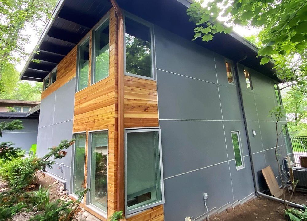 Modern gray house with wood accents and large windows, nestled in greenery