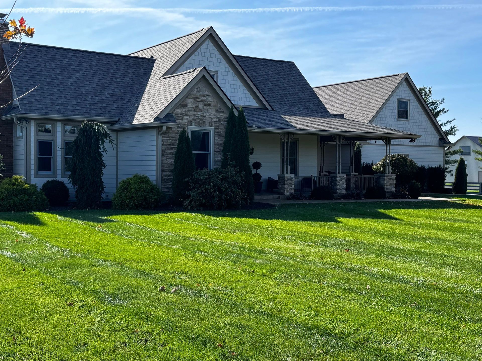 Single-story house with gray roof and white siding, front porch, and a bright green lawn under a blue sky