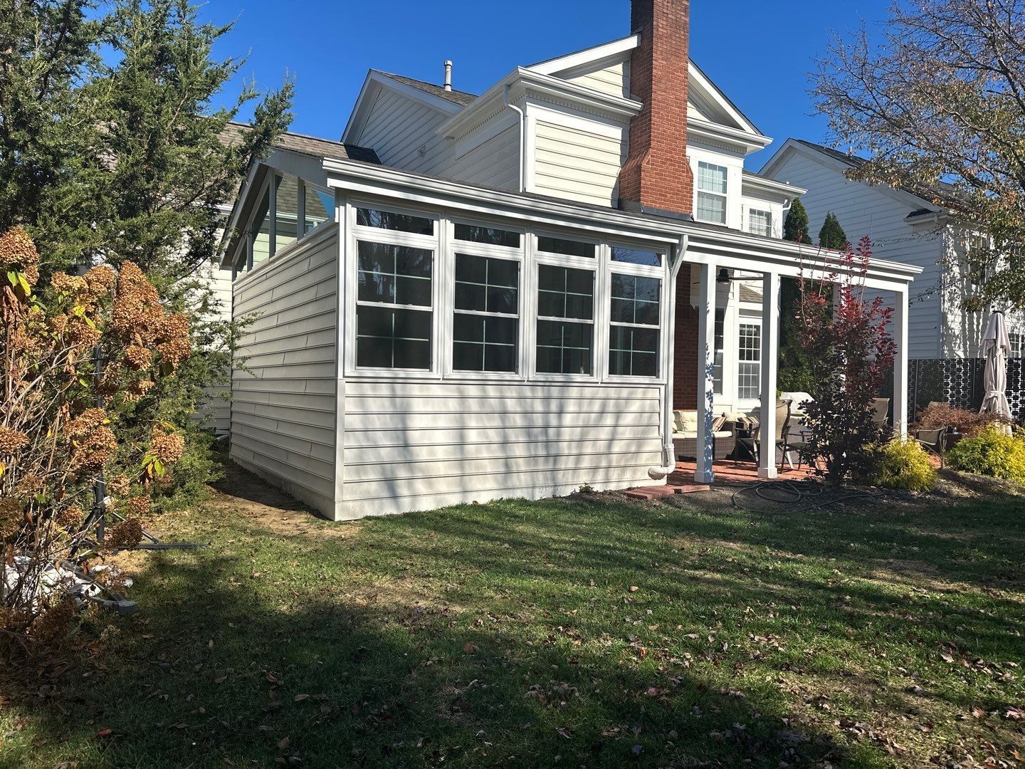 White house with screened porch and red brick chimney in a leafy yard on a sunny day