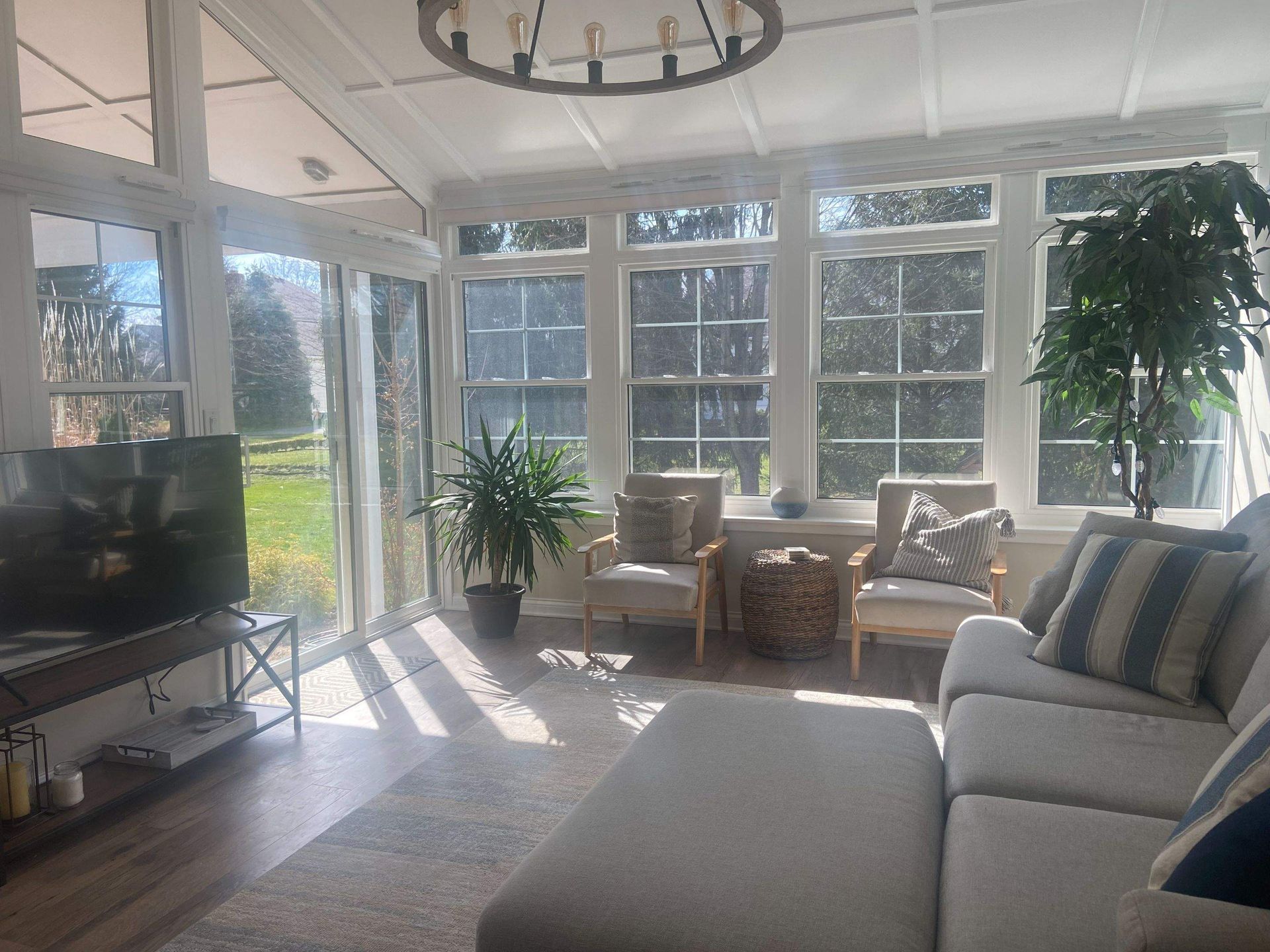 Bright sunroom with white furniture, large windows, a TV, and sunlight streaming across the floor.