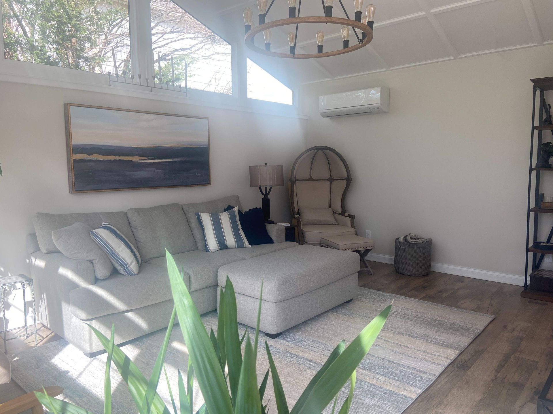 Bright living room with gray sectional, striped pillows, wall art, rug, and sunlight from large windows.
