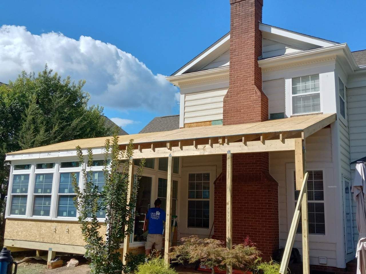 House with a brick chimney and covered porch under construction on a sunny day
