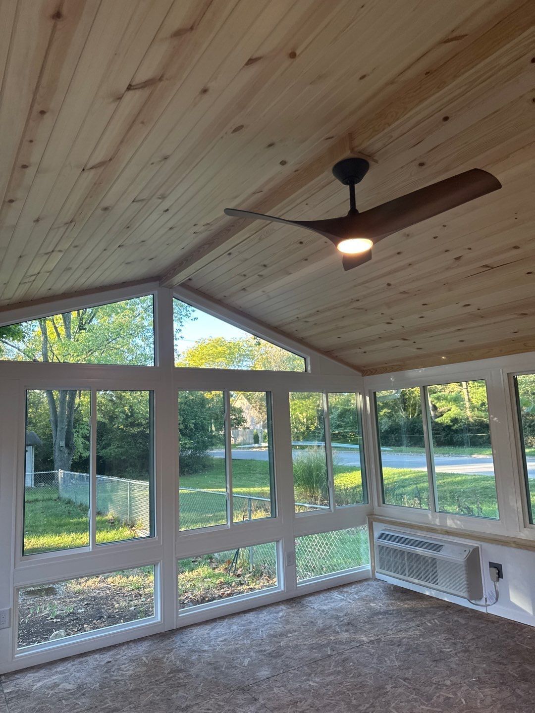 Sunroom with vaulted wood ceiling, ceiling fan, carpet, and large windows overlooking a green yard.