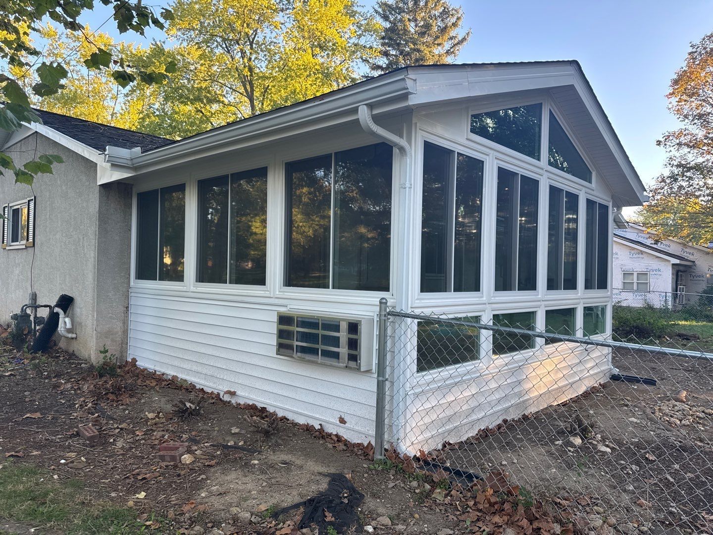 Enclosed porch with white siding and large windows attached to a house in a wooded yard