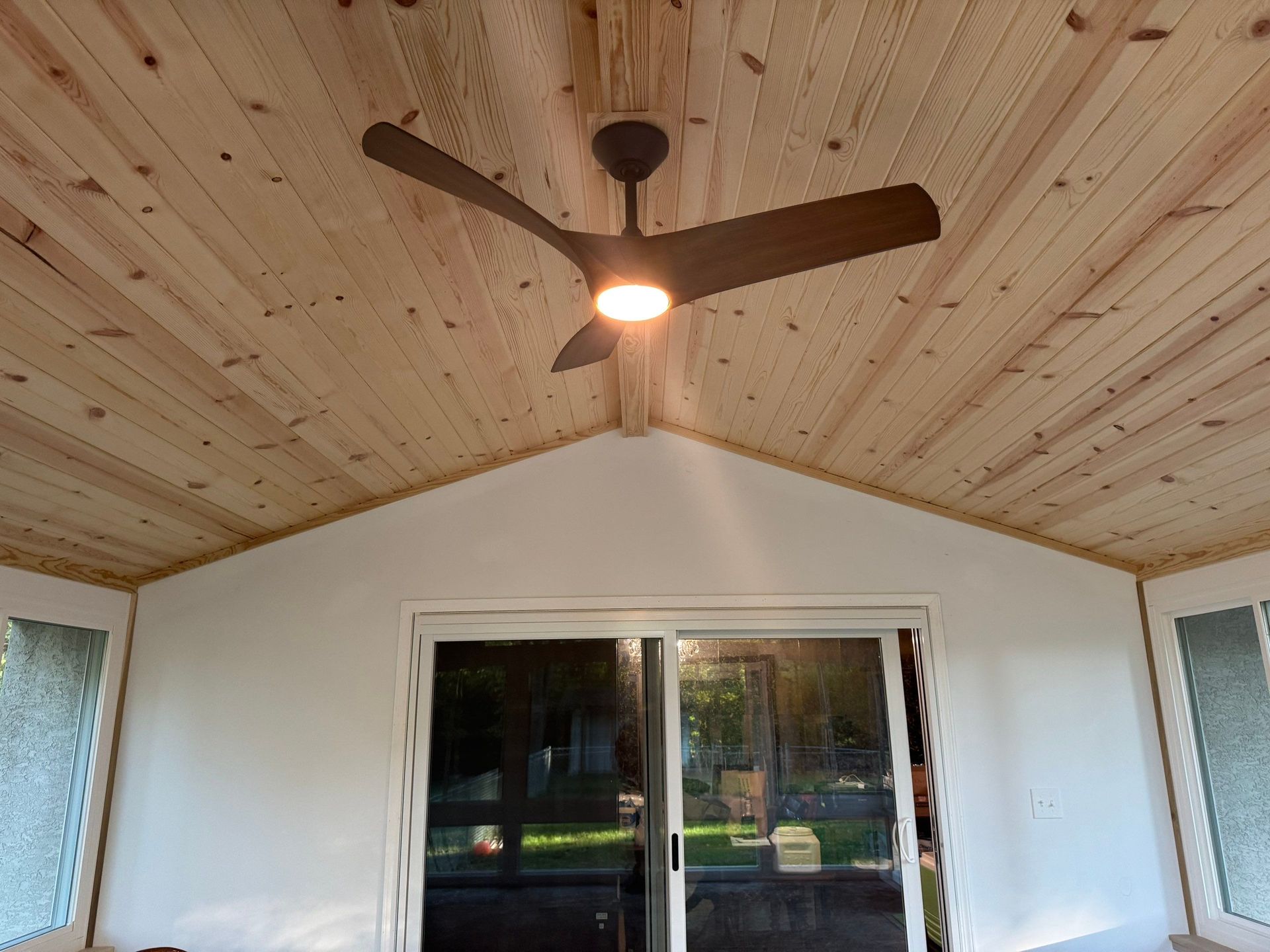 Covered patio ceiling with a lit ceiling fan above sliding glass doors