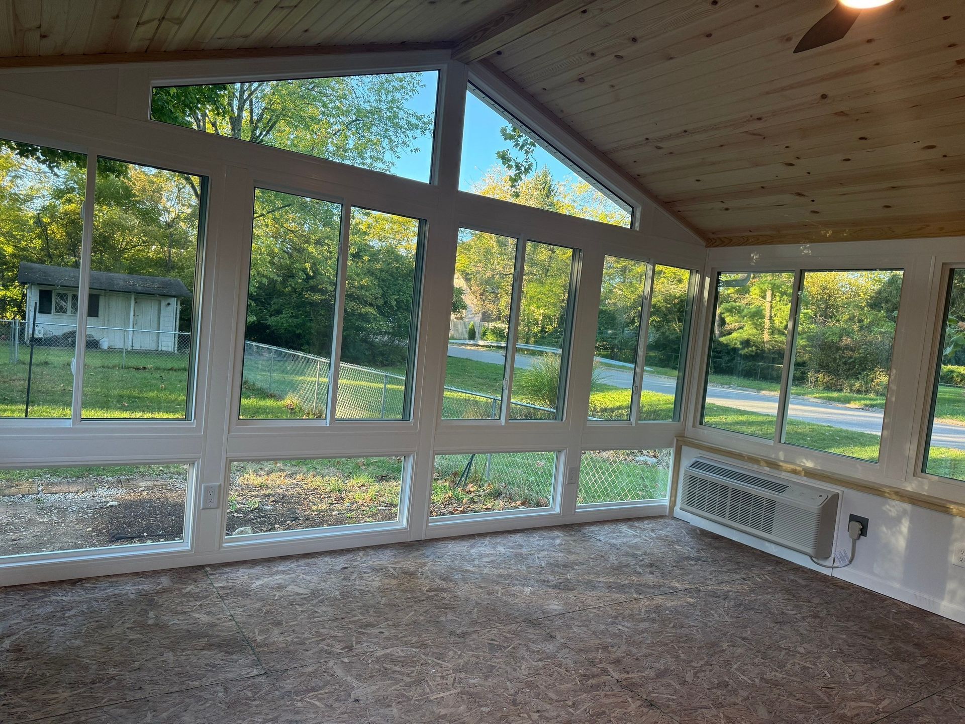 Empty sunroom with large windows overlooking a grassy yard and trees