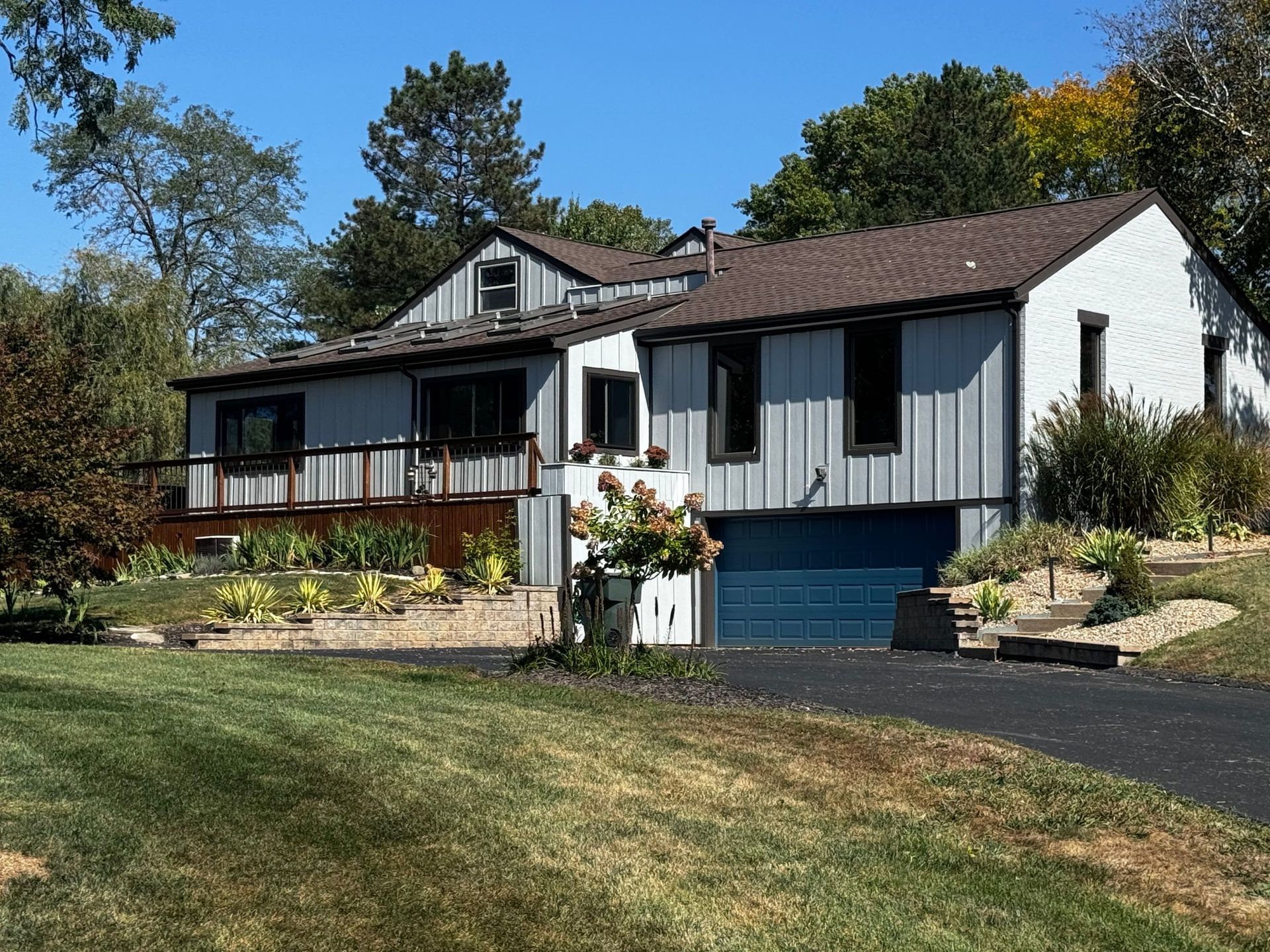 Suburban house with white siding, blue trim, and a front garden on a sunny hillside.
