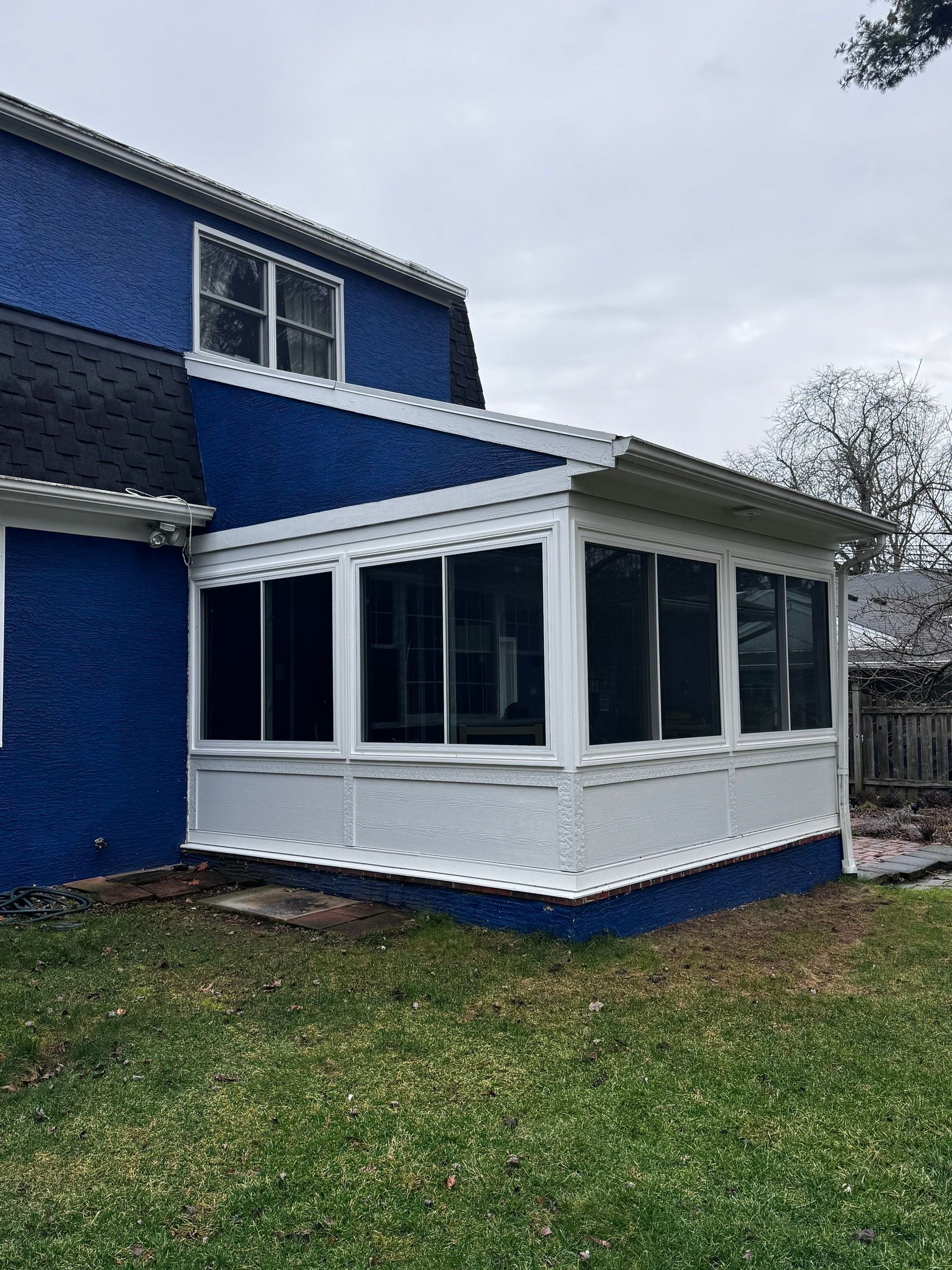 Blue house with white screened porch and windows, viewed from the yard under an overcast sky