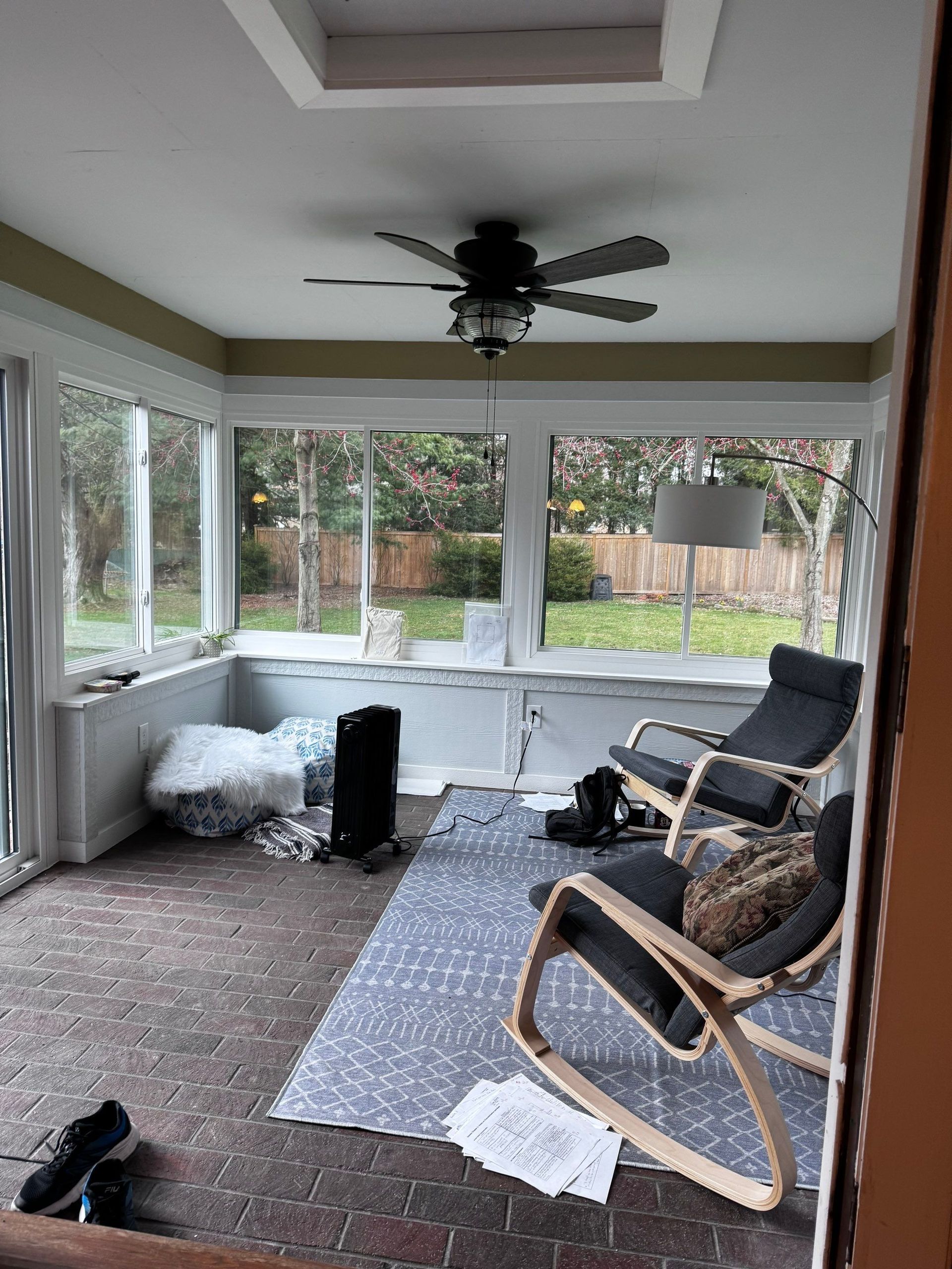 Enclosed porch with windows, ceiling fan, rug, lounge chairs, and outdoor view.