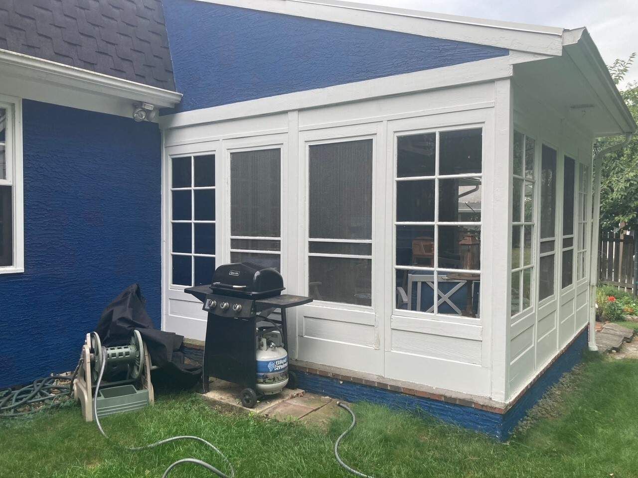 Blue house sunroom with white trim, screened windows, and a grill on the grass beside it