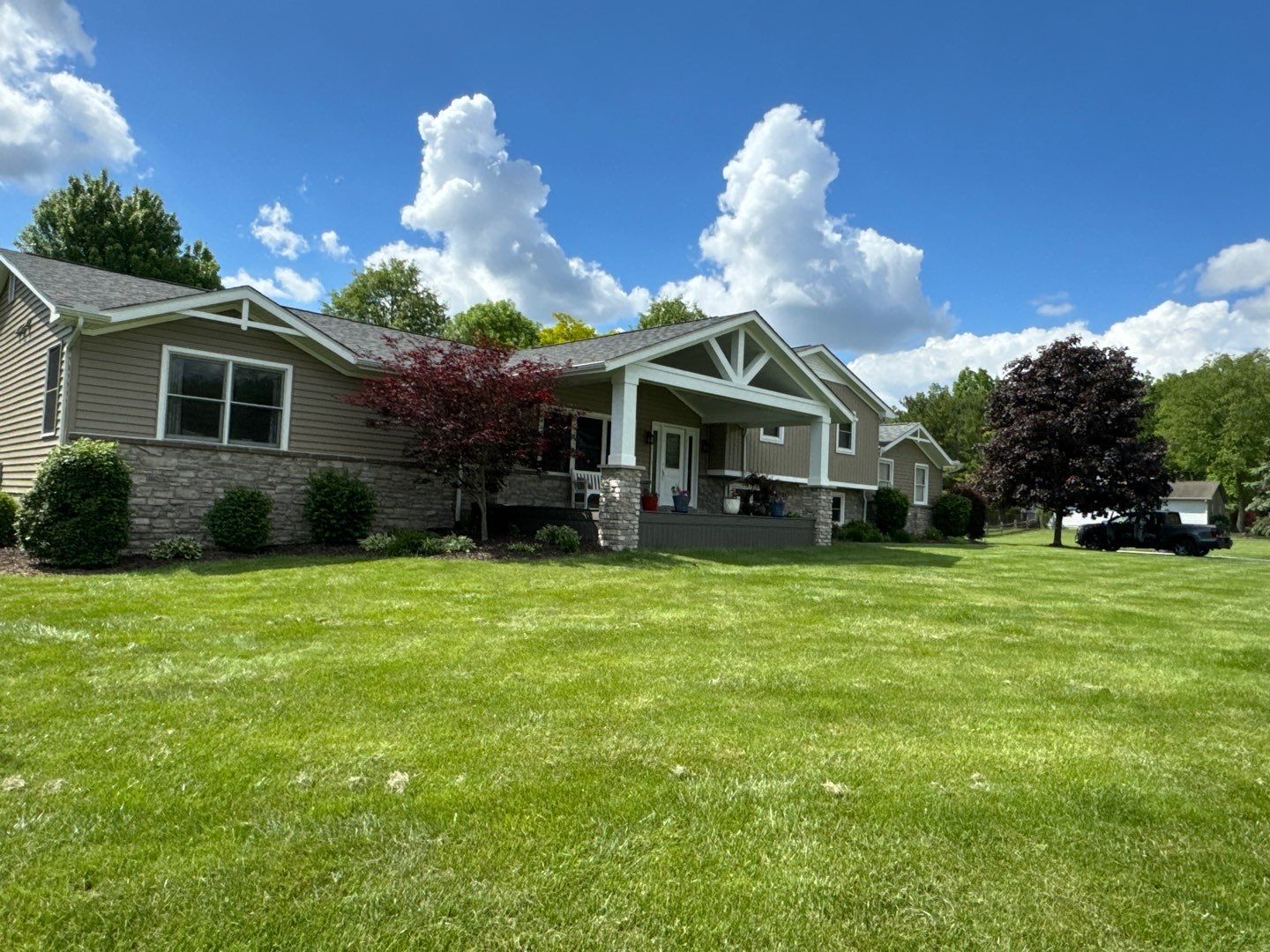 Suburban house with stone exterior, white porch, and large green lawn under a blue sky