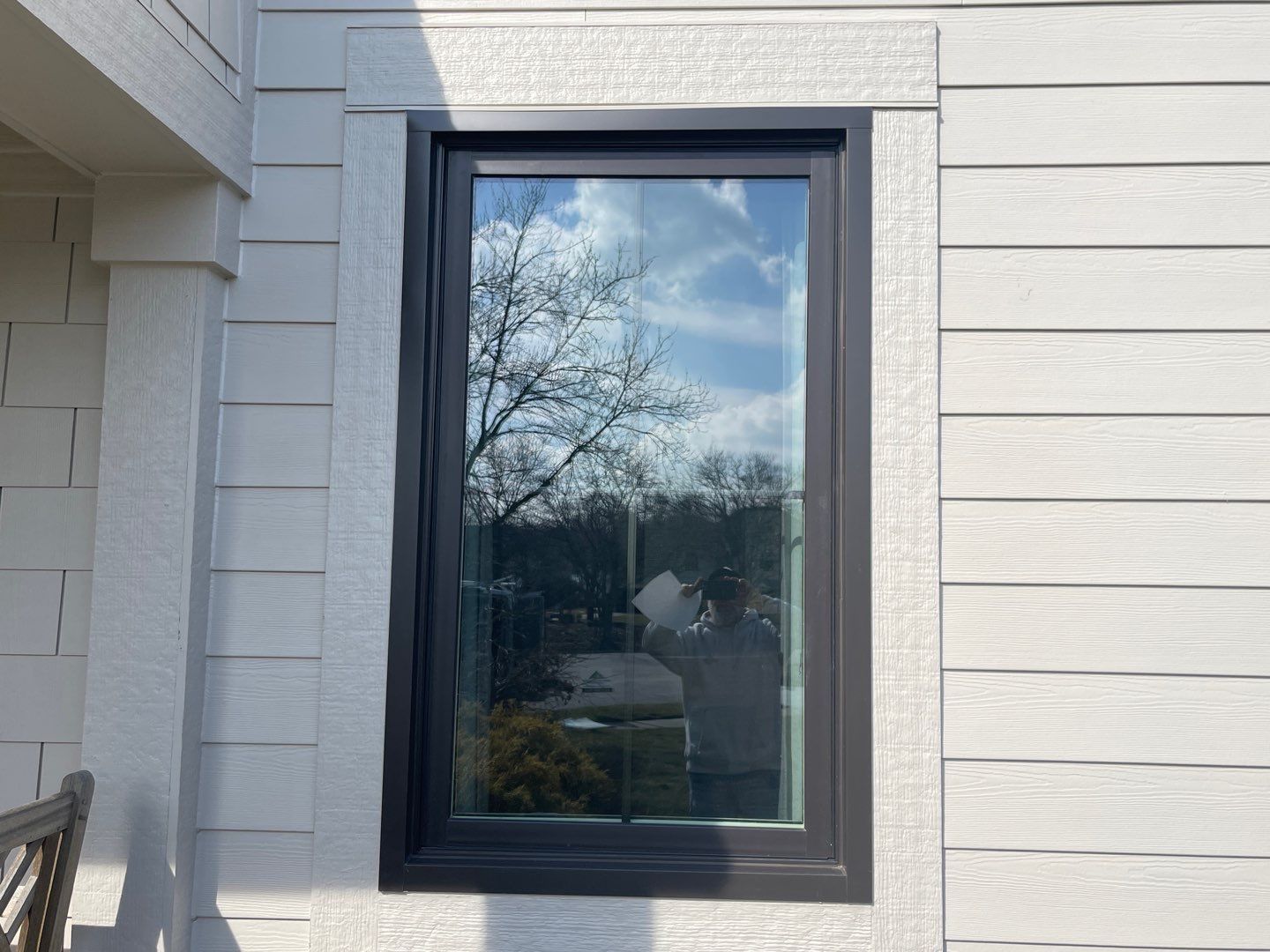 Black-framed window on a white exterior wall reflecting trees and sky
