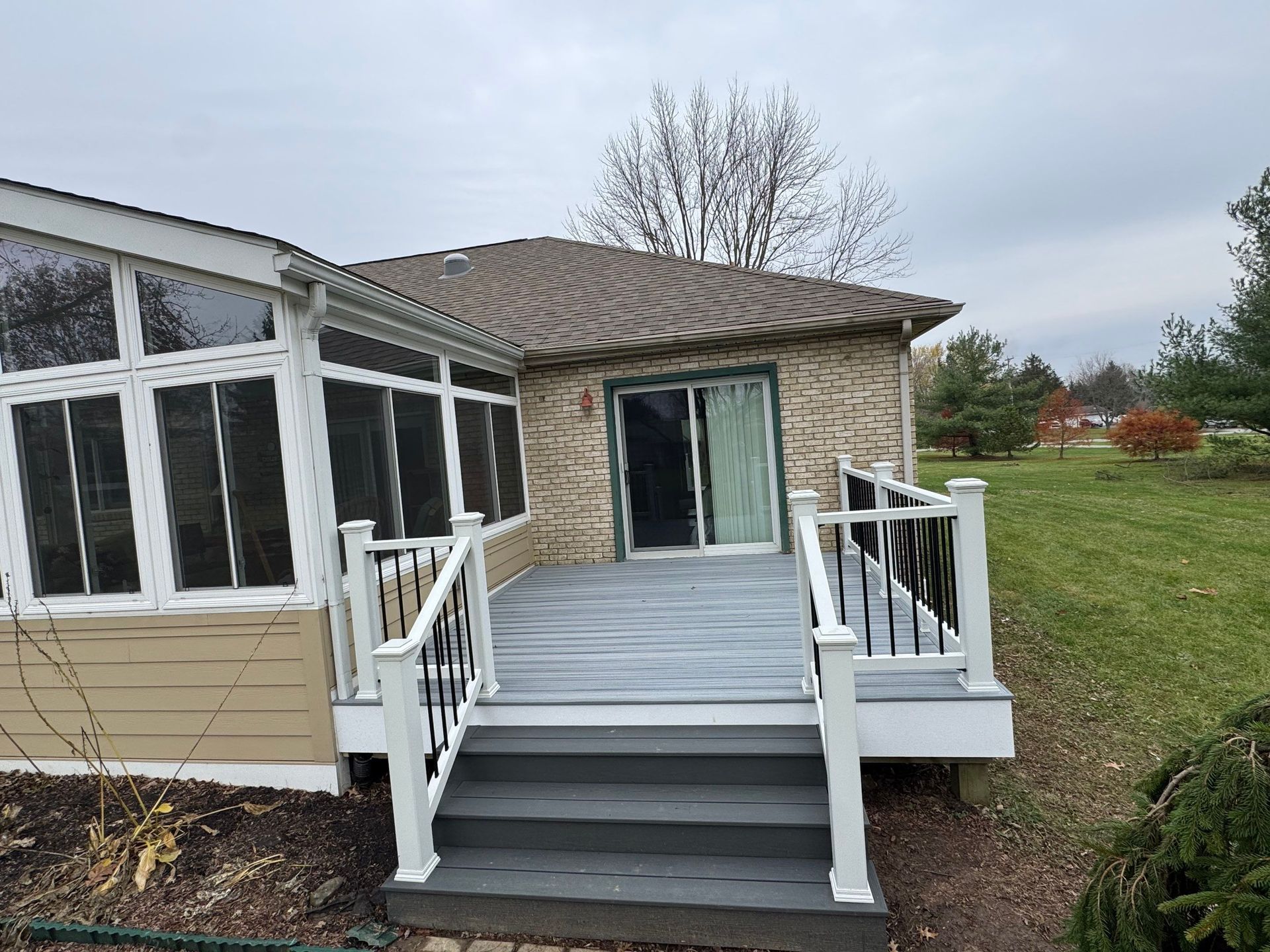 Deck with white railings and steps leading to a screened porch on a beige house.