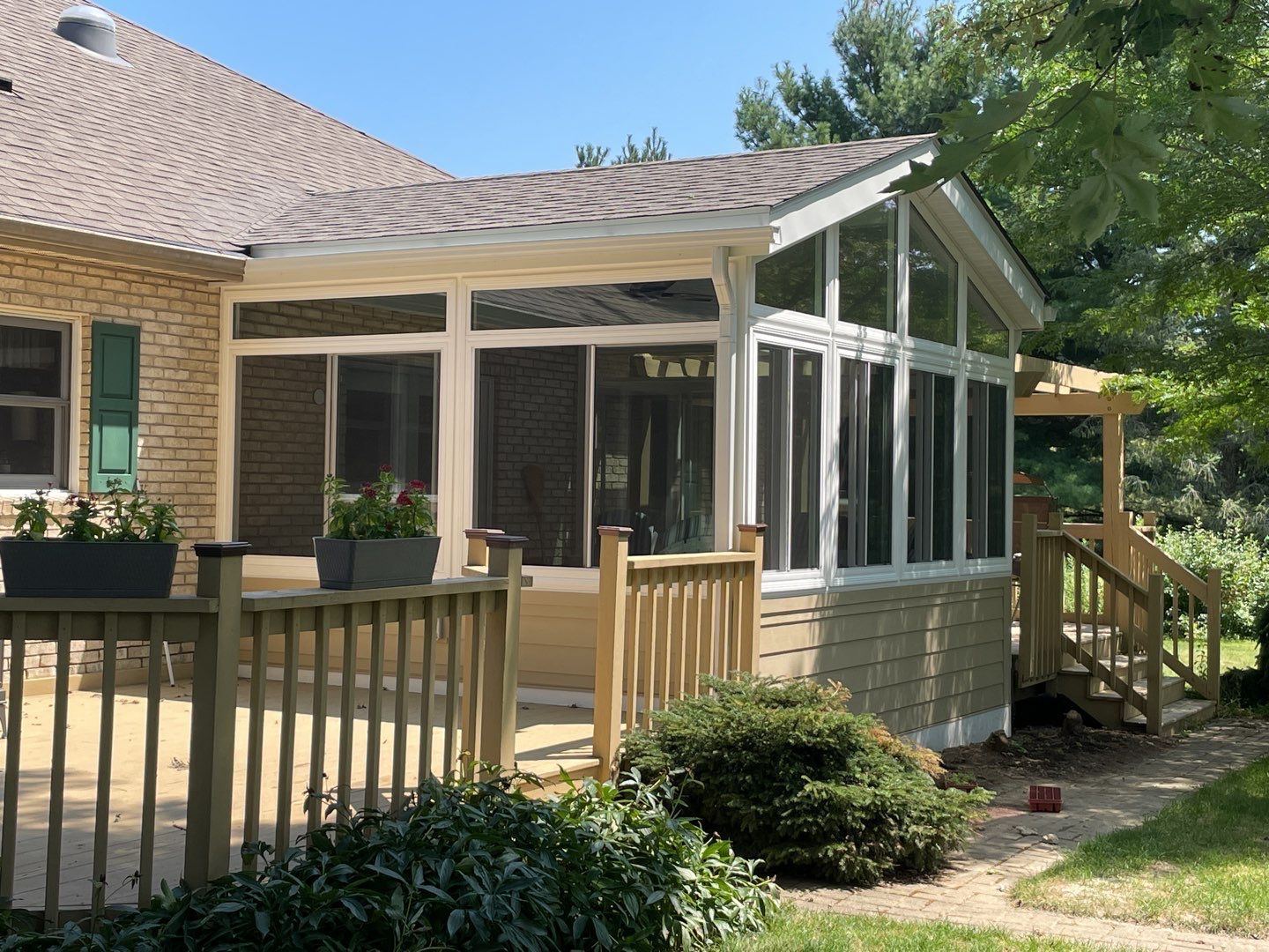 Screened-in porch with sliding glass doors and wooden railing on a house in a sunny yard