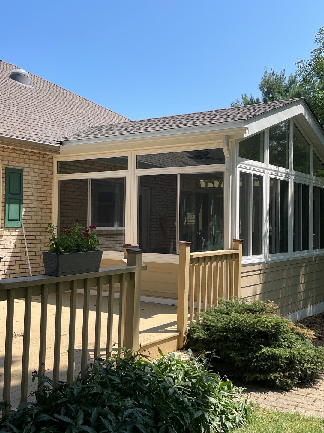 Backyard patio with covered porch, brick house, wooden deck, and screened windows under a clear blue sky