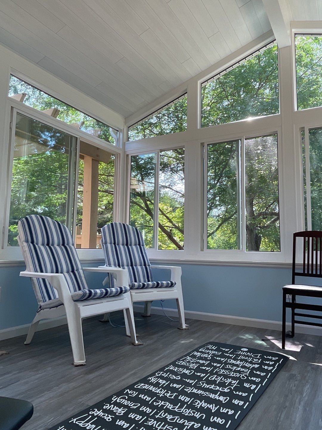 Sunroom with two striped chairs, large windows, and a patterned rug looking out onto green trees.