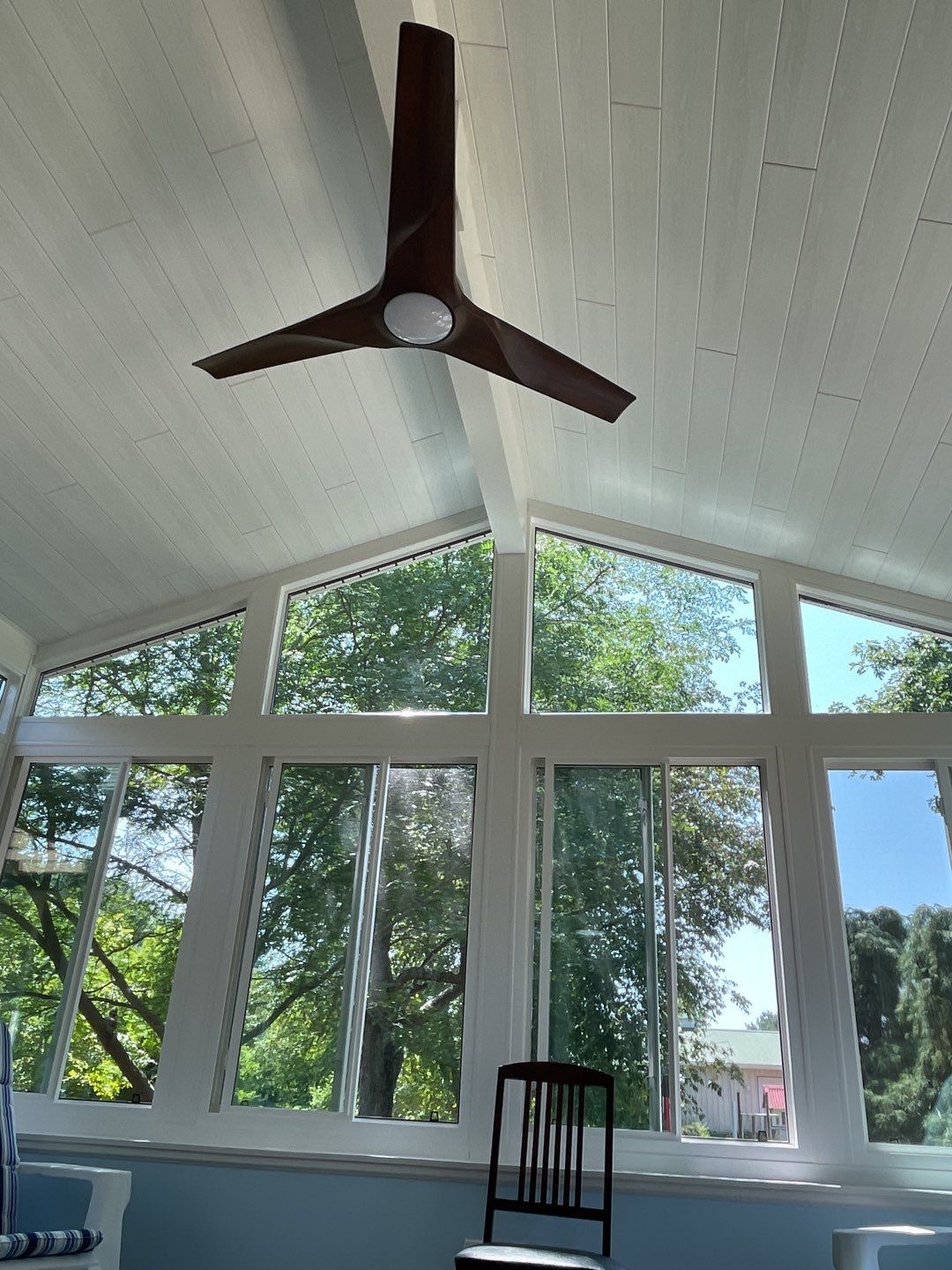 Bright living room with vaulted windows, ceiling fan, and trees visible outside