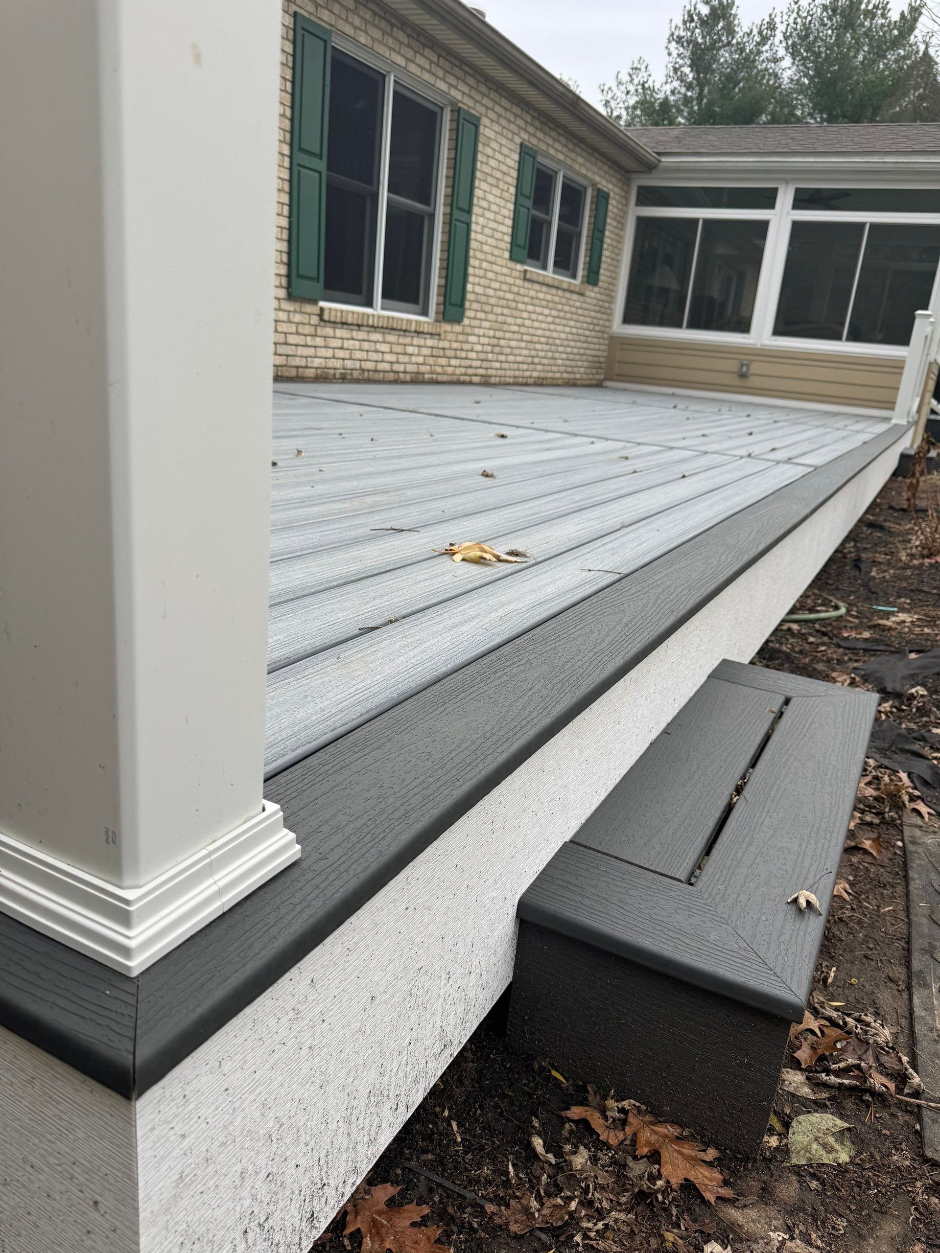 Raised white deck with black trim beside a house, with a gray step block and screened porch in the background
