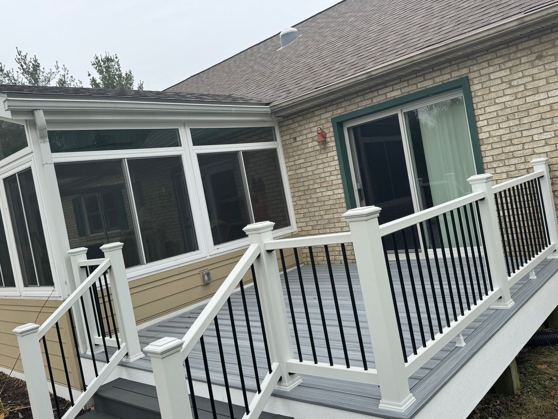 Snow-covered backyard deck with white railings and black balusters beside a house