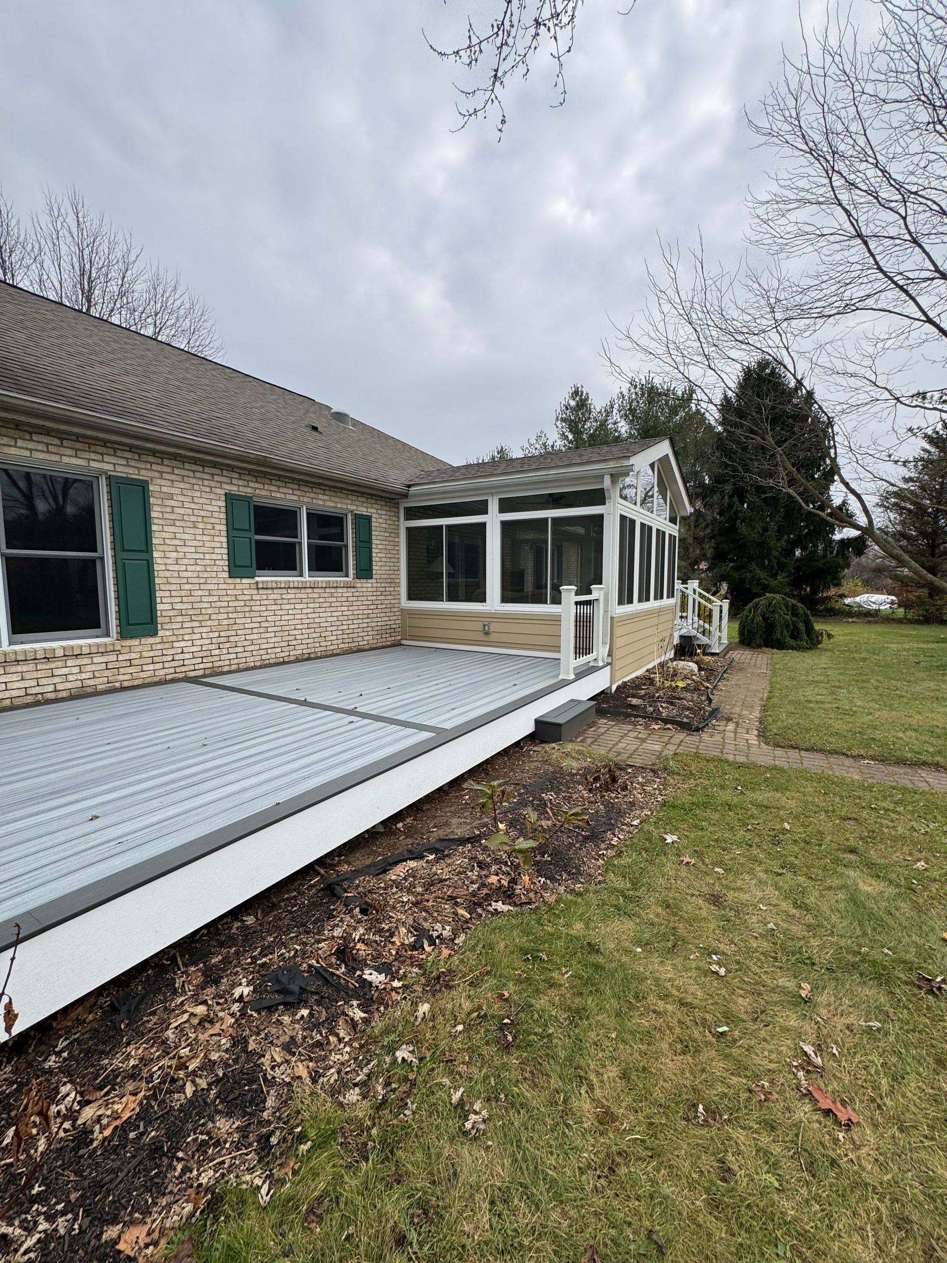 Stone house with a white ramp and screened porch beside a grassy yard under cloudy skies