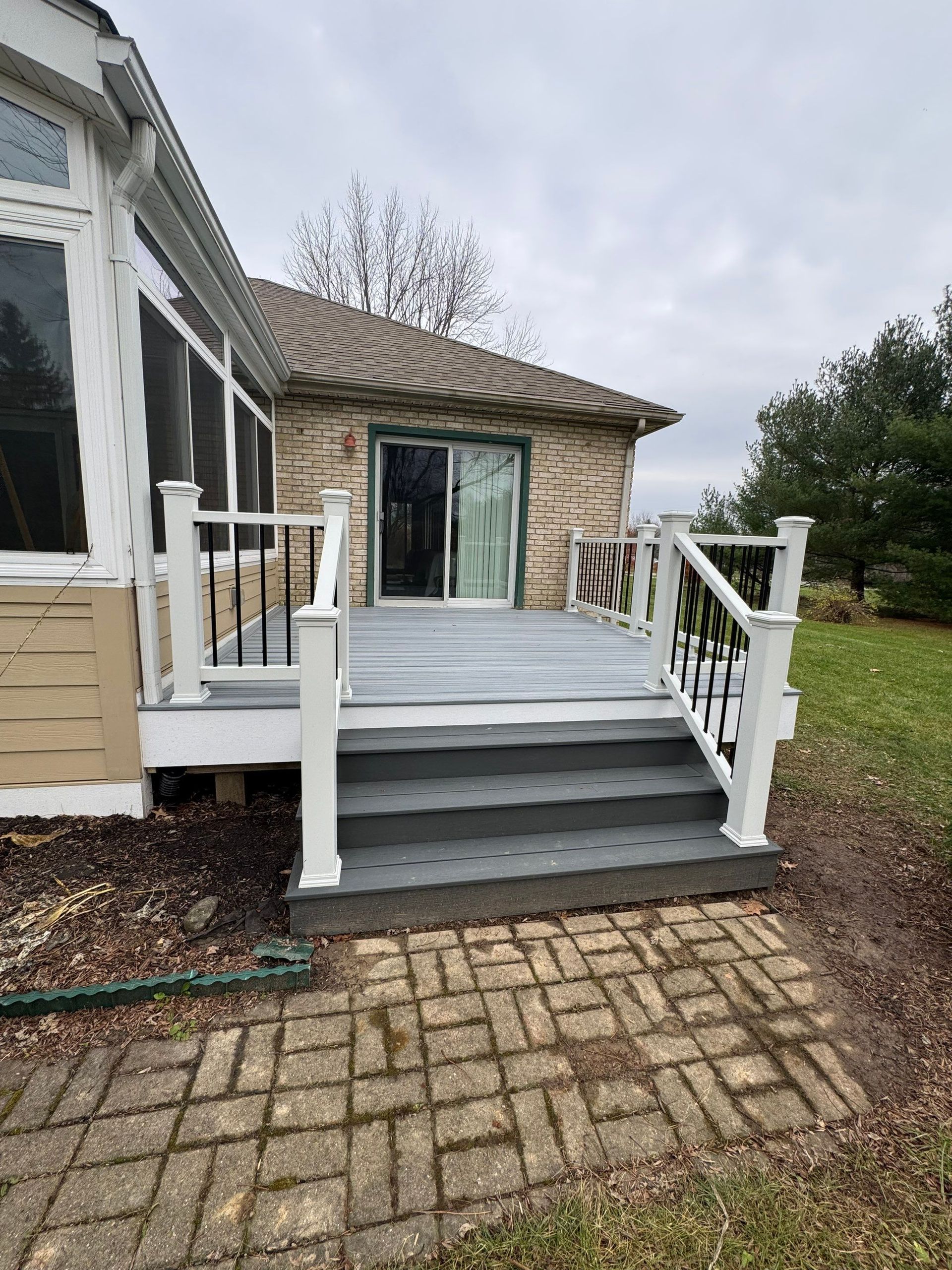 Front porch with white railings, gray steps, and sliding glass doors on a brick house.