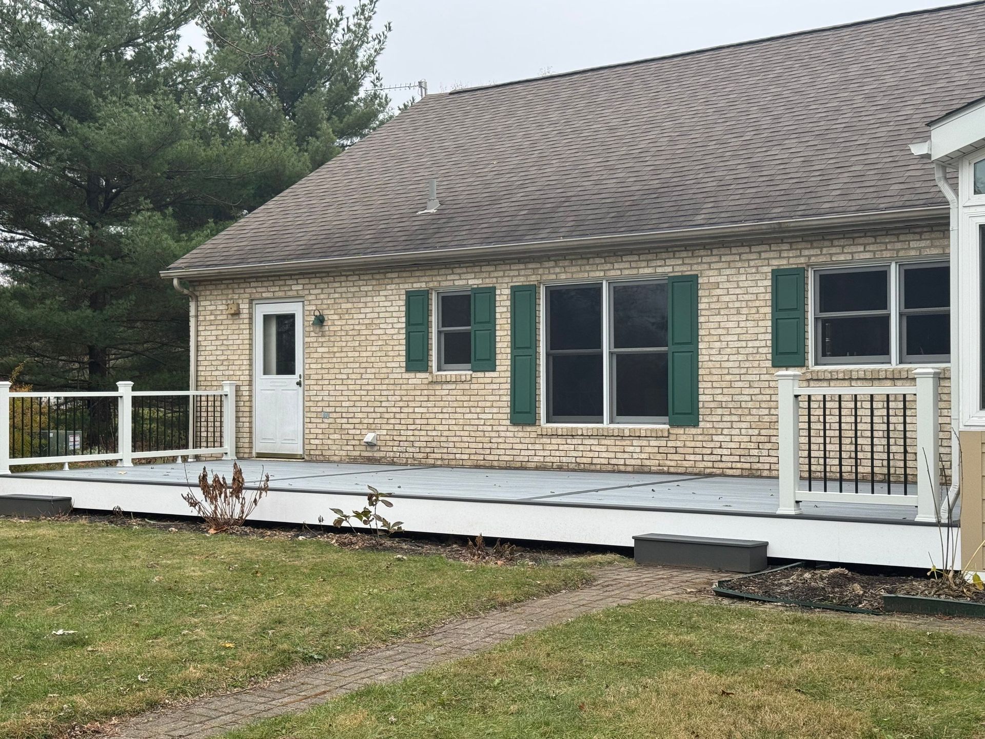 Front view of a stone house with a curved shingle roof and white porch railing, set in a grassy yard.