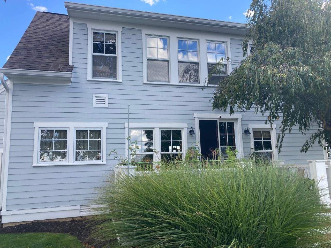 Two-story light gray house with white trim and large green shrub in front yard