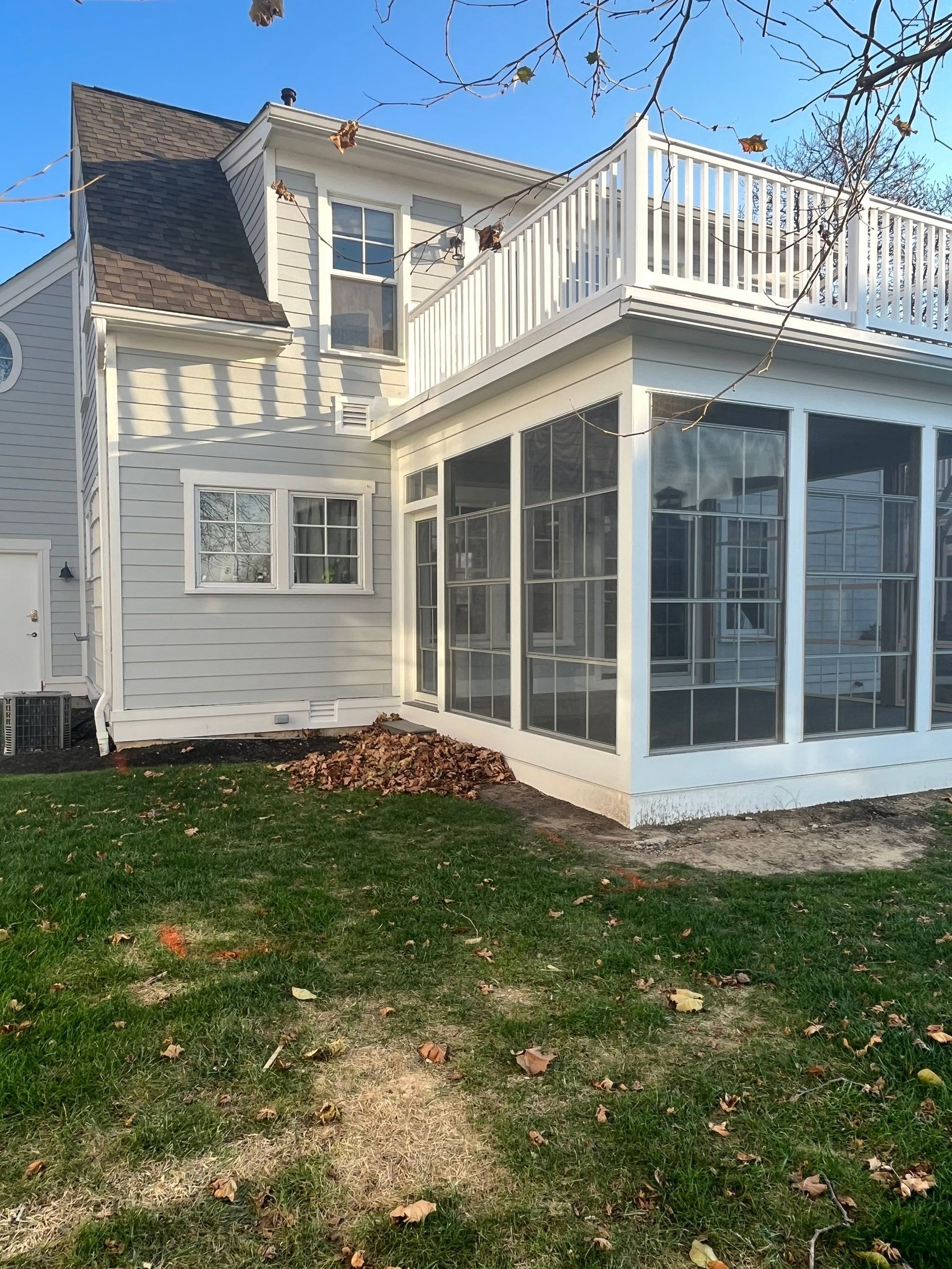 White two-story house with screened porch and rooftop deck, viewed from the backyard.