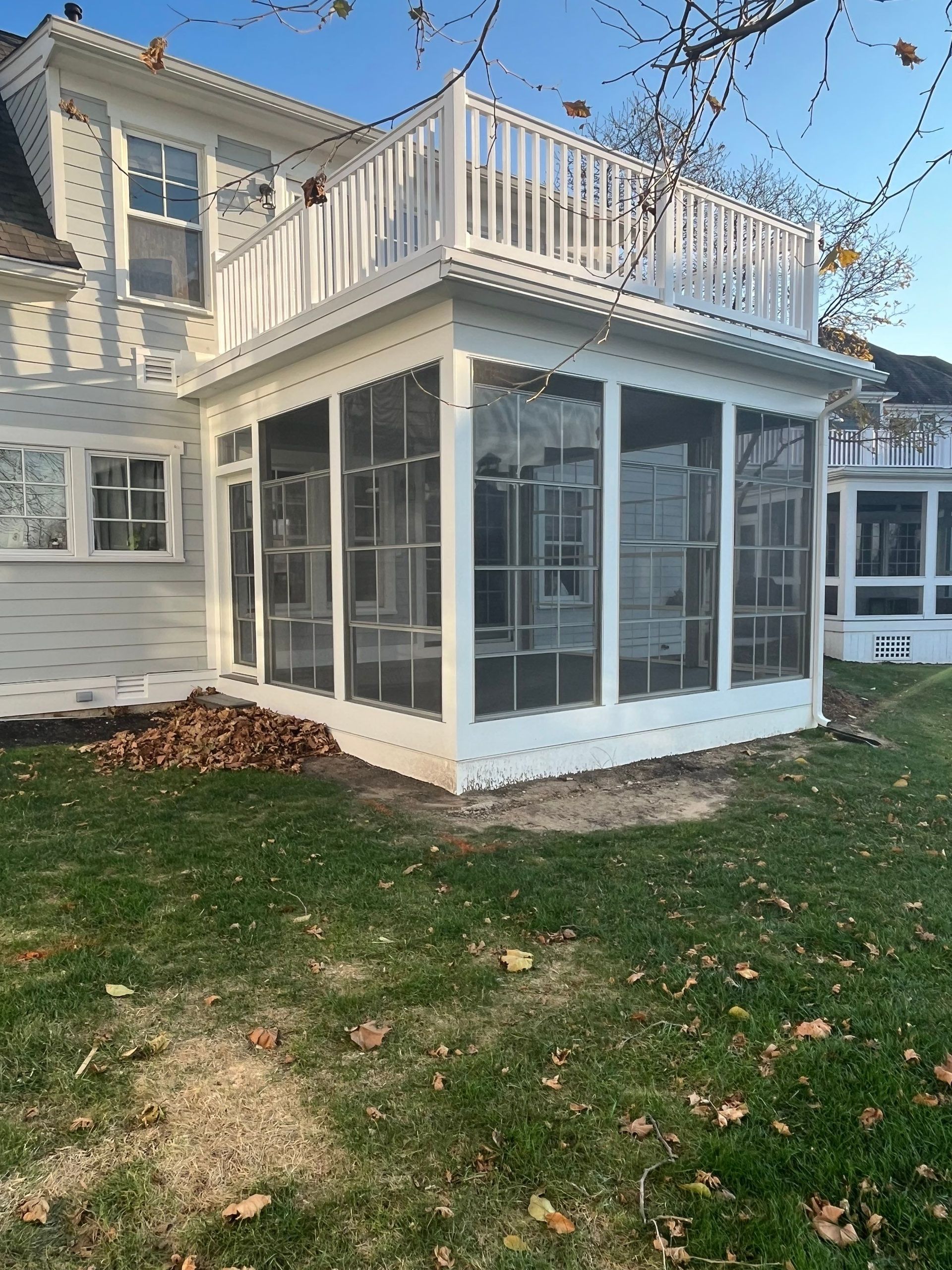 White house sunroom with screened windows and upper deck, viewed from the backyard lawn