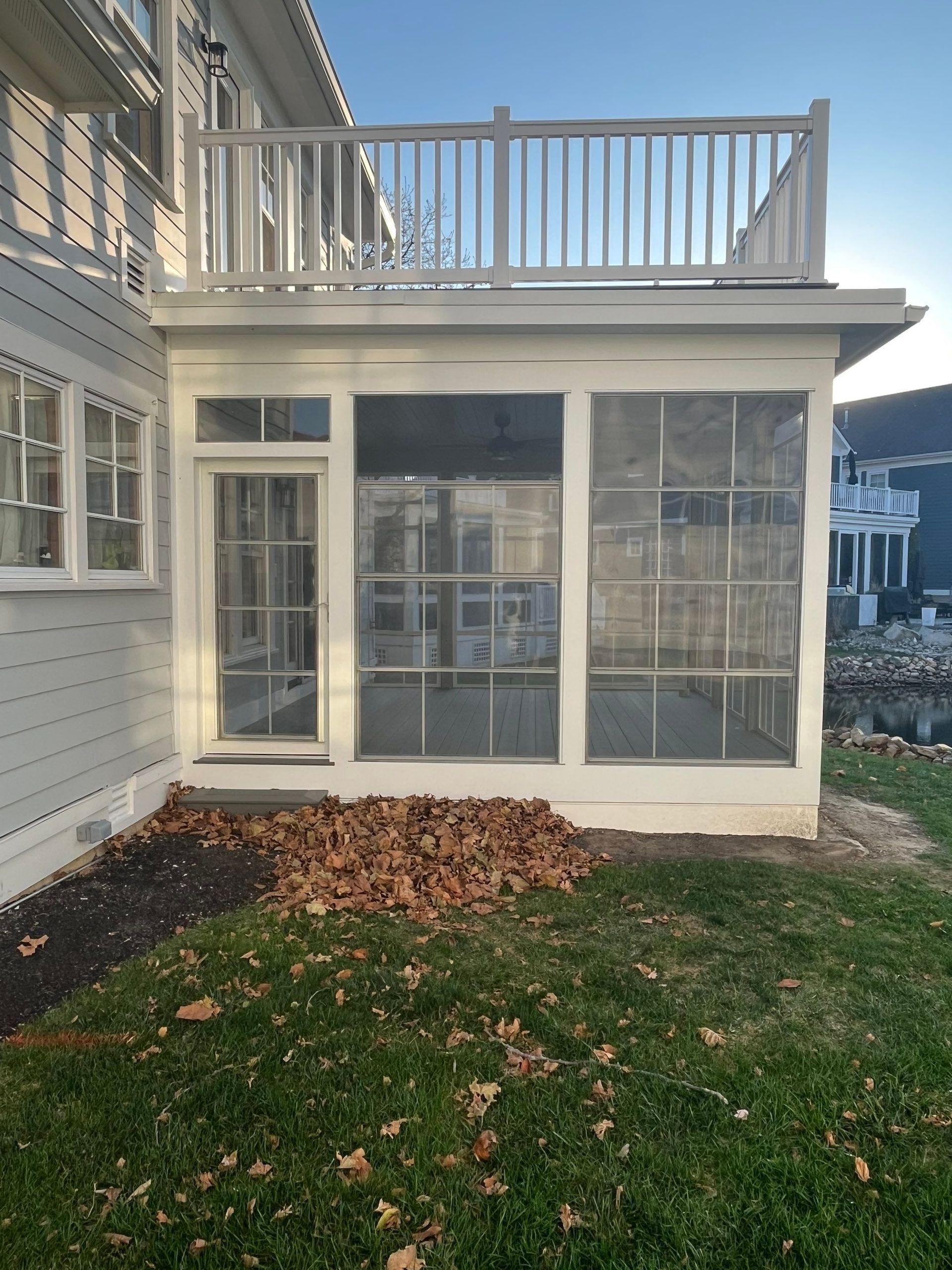 Back porch sunroom with white siding, screened windows, and a small lawn with fallen leaves