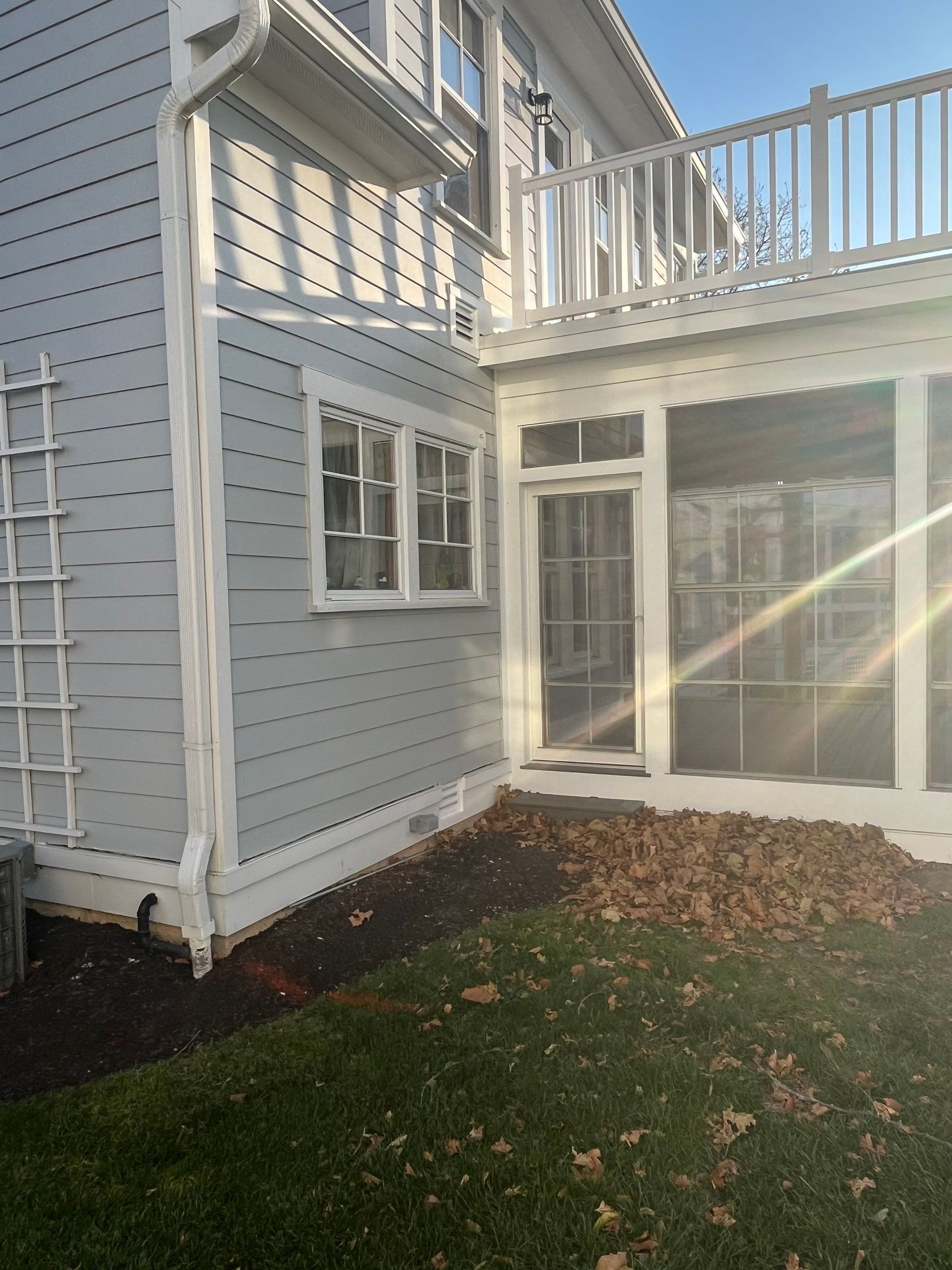 White house exterior with deck, sliding glass door, windows, and a small grass yard with leaves
