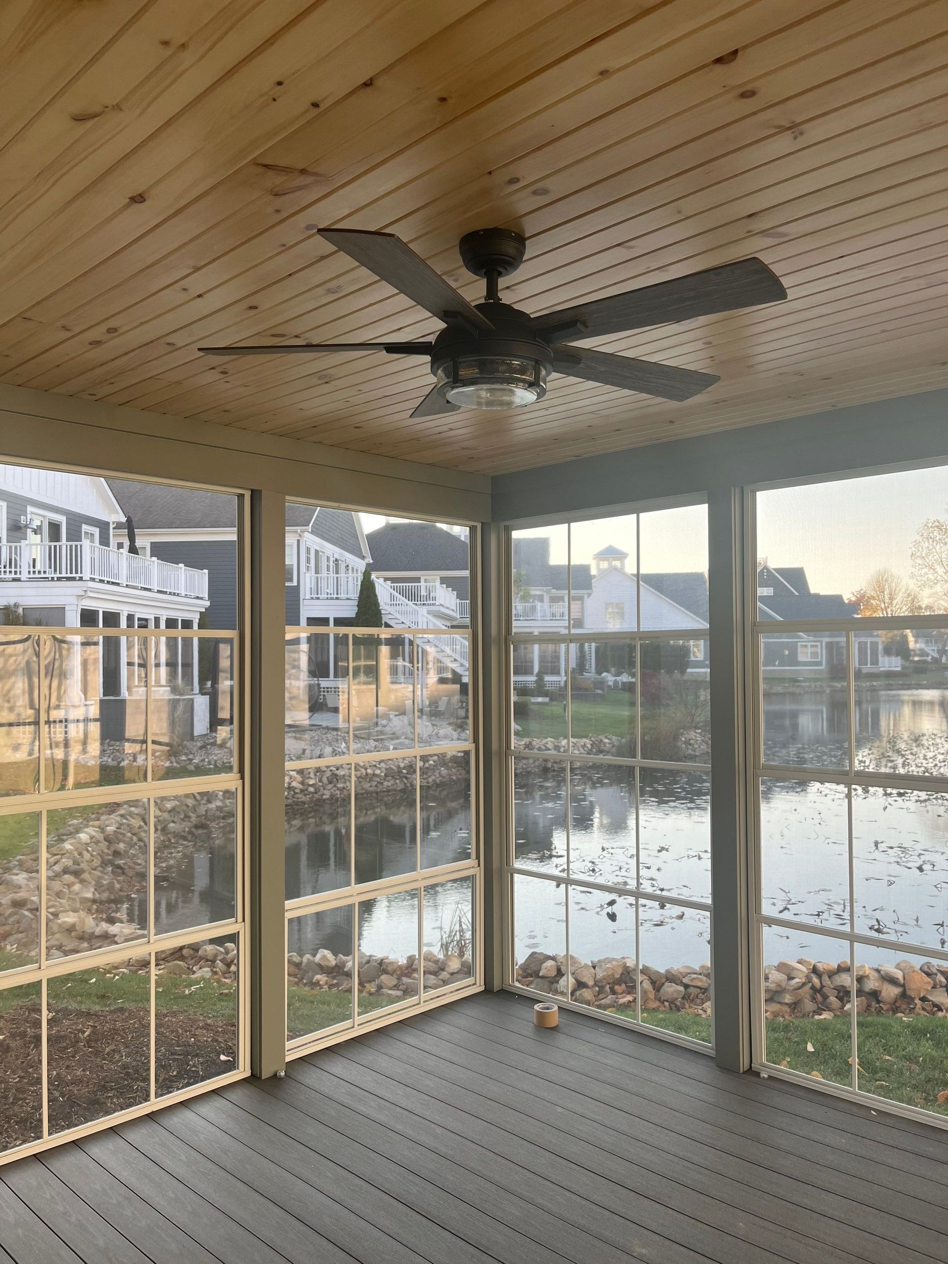 Screened porch with ceiling fan overlooking a pond and neighboring homes at sunset