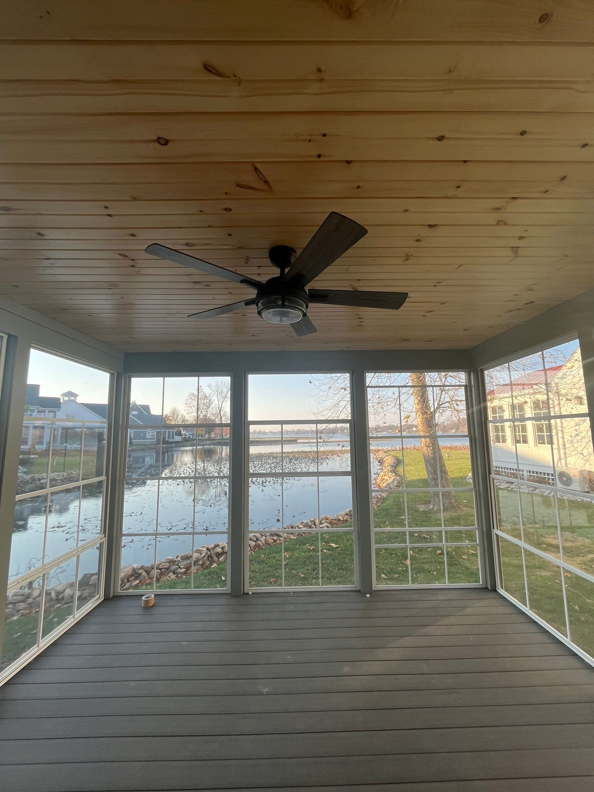 Enclosed porch with wood ceiling, fan, large windows, and a view of water and houses outside