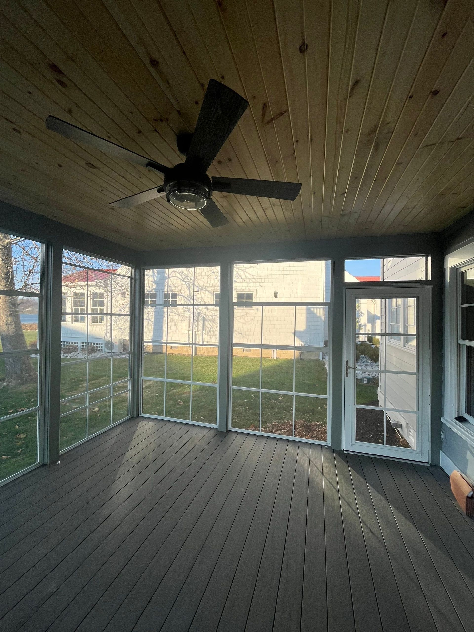 Empty screened-in porch with dark wooden floor, wood ceiling, ceiling fan, and windows overlooking outdoors