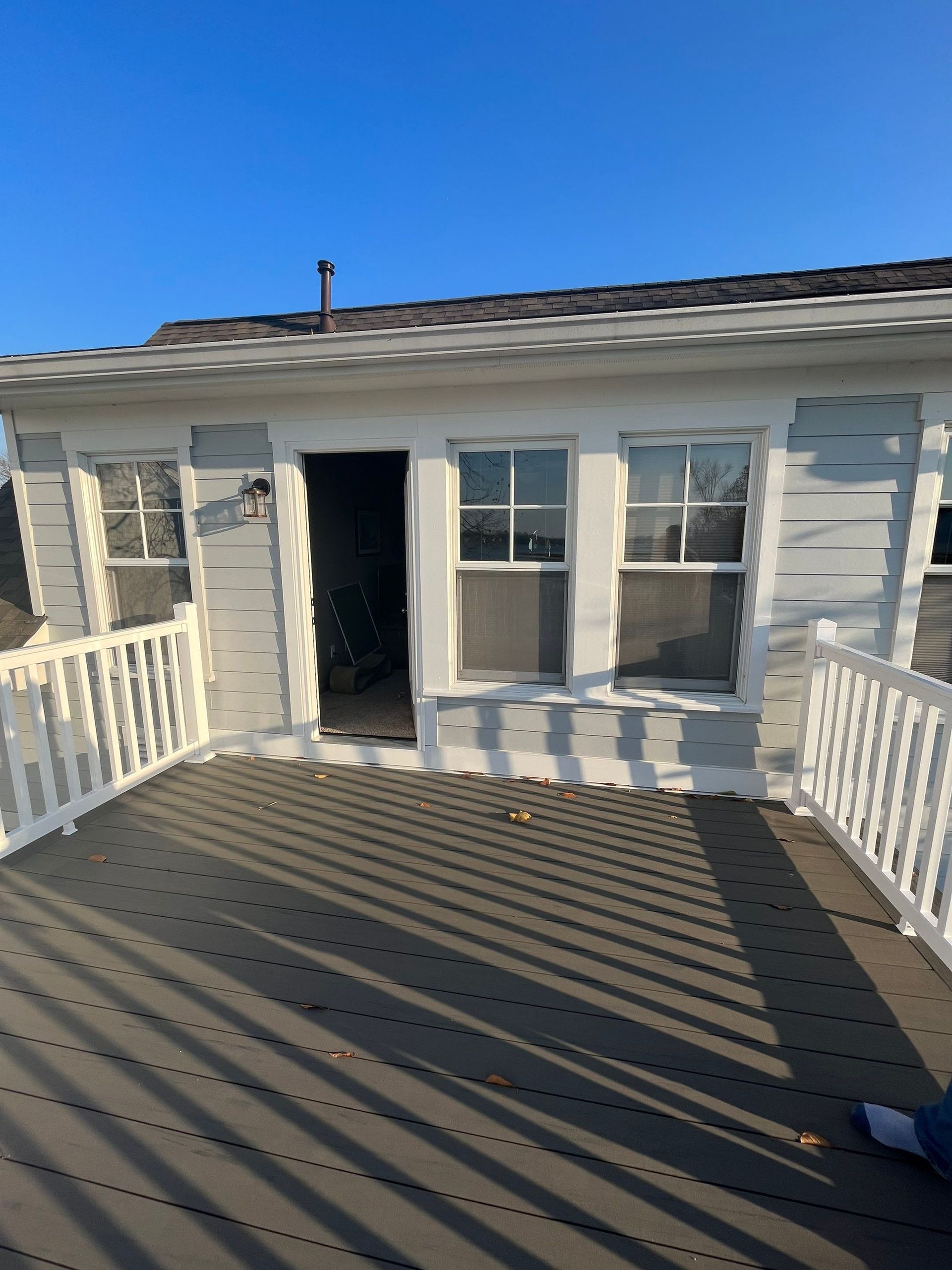 White house porch with gray deck, white railings, and an open front door under a clear blue sky
