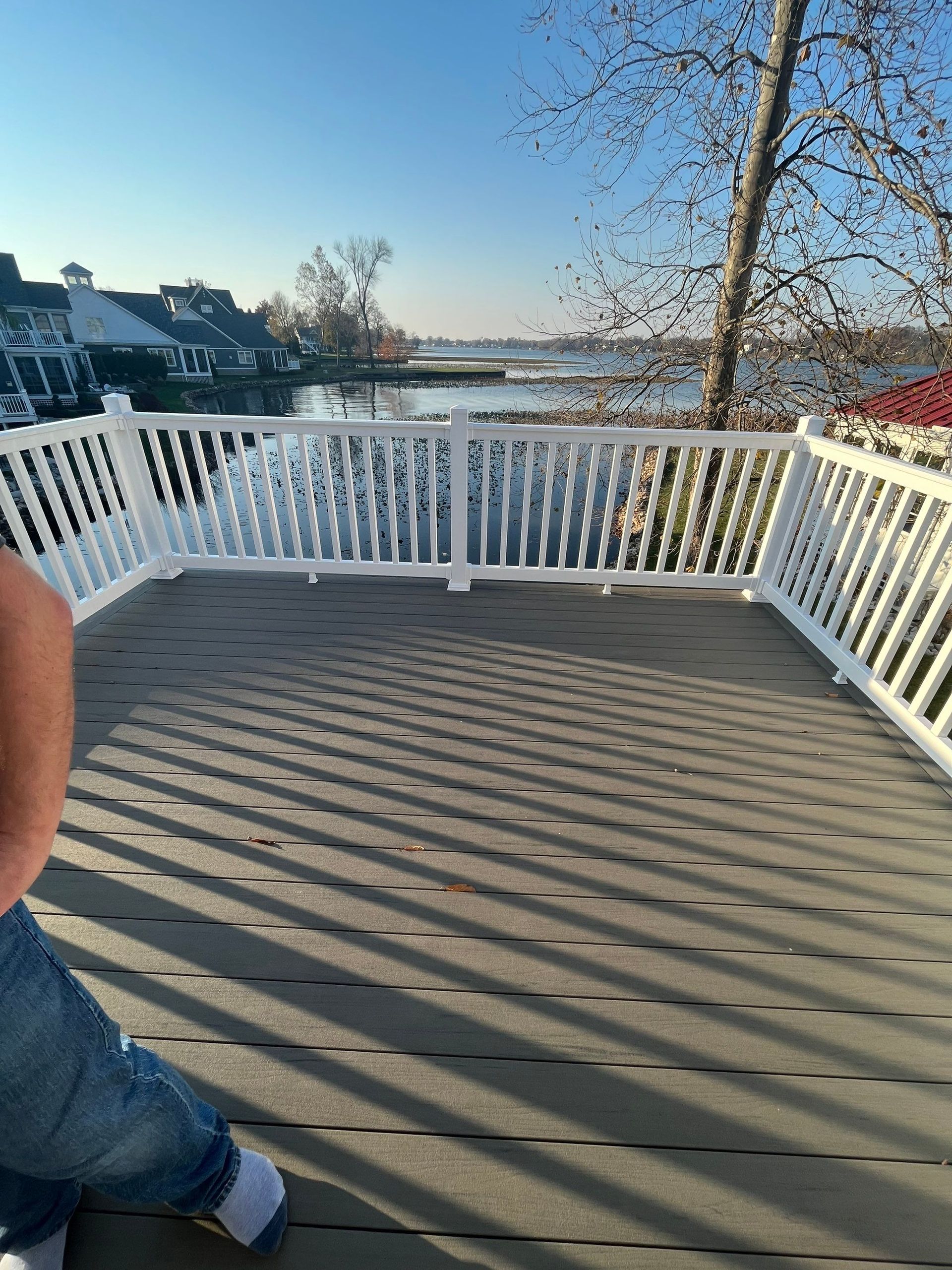 Wooden deck with white railing overlooking a snowy waterfront at sunset, with part of a person visible on the left.