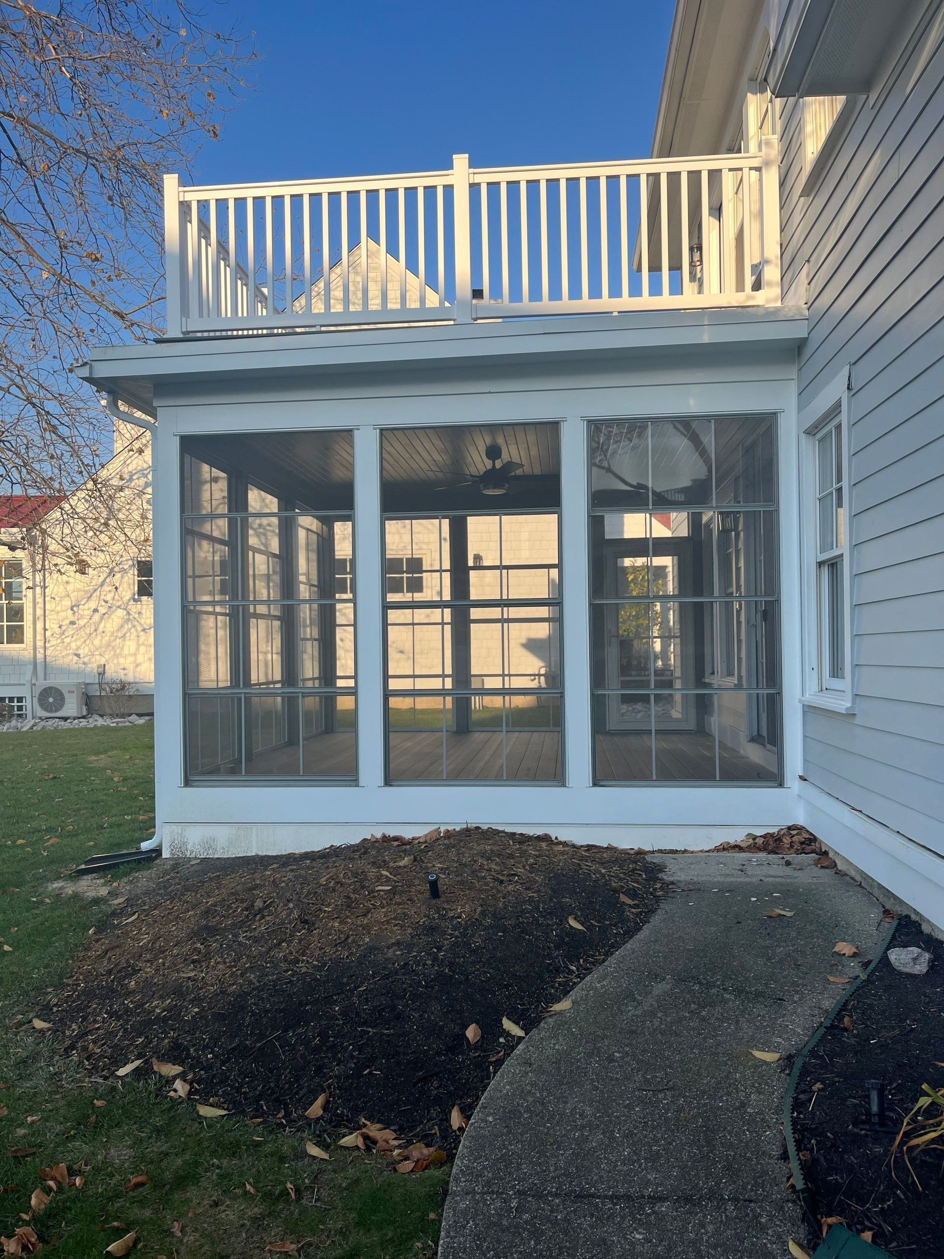 Back patio with glass sunroom, white siding, and deck railing above at dusk