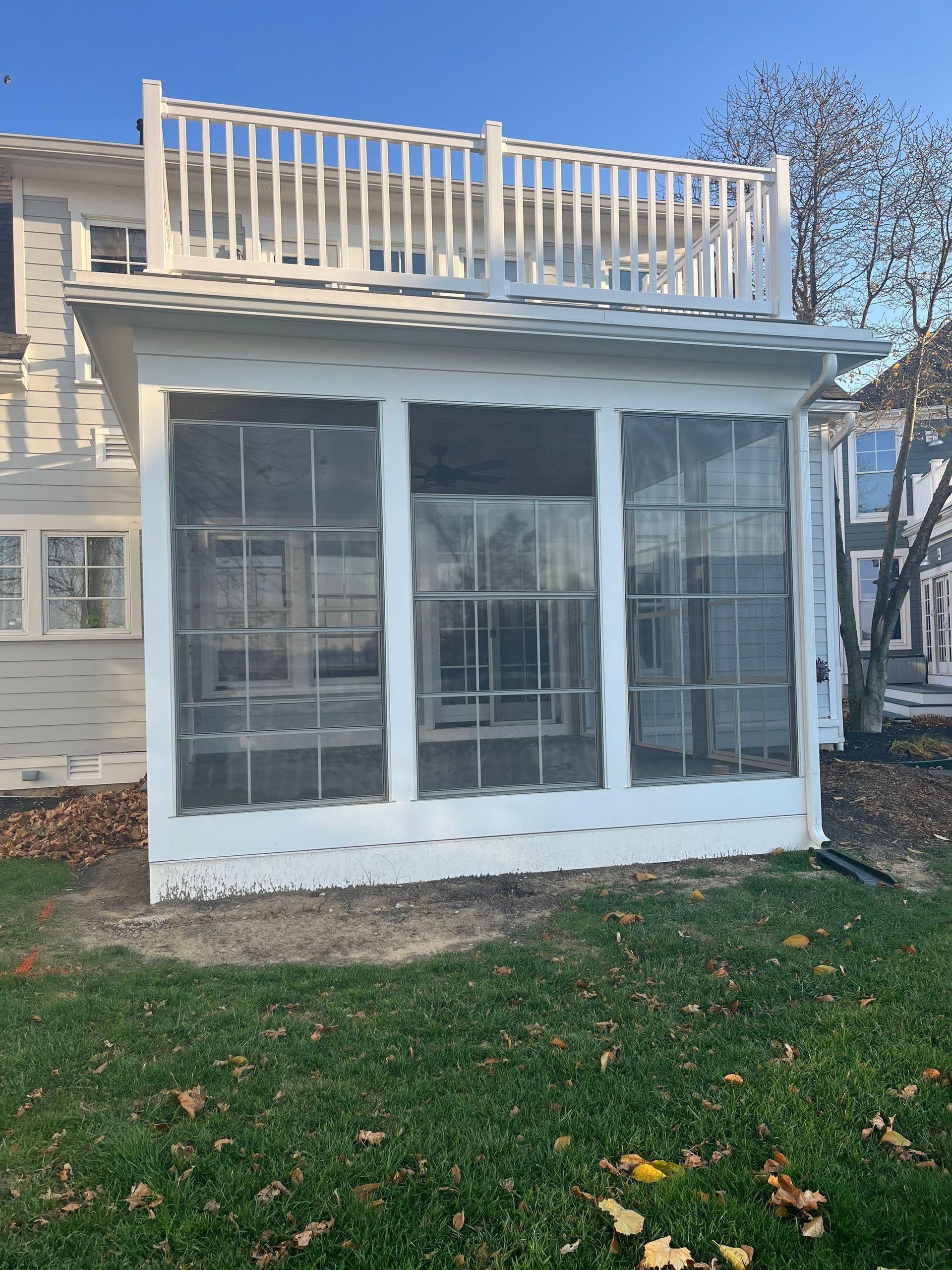 White enclosed porch or sunroom on a house with large windows and a rooftop deck.
