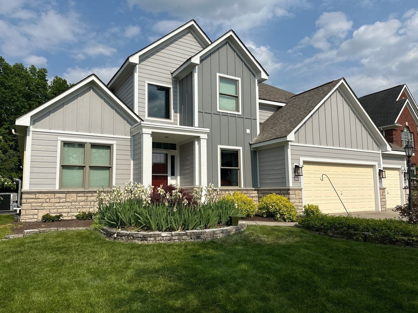 Gray suburban house with white trim, two-car garage, and a green lawn under a blue sky