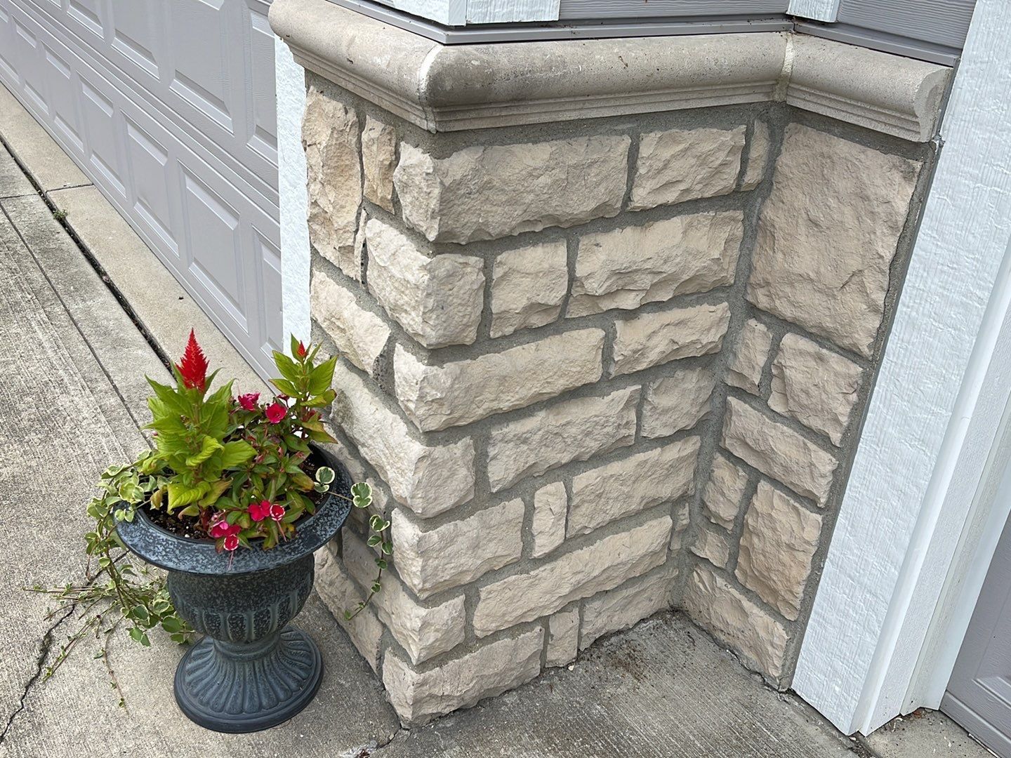 Potted red flowers beside a stone house corner and white garage door