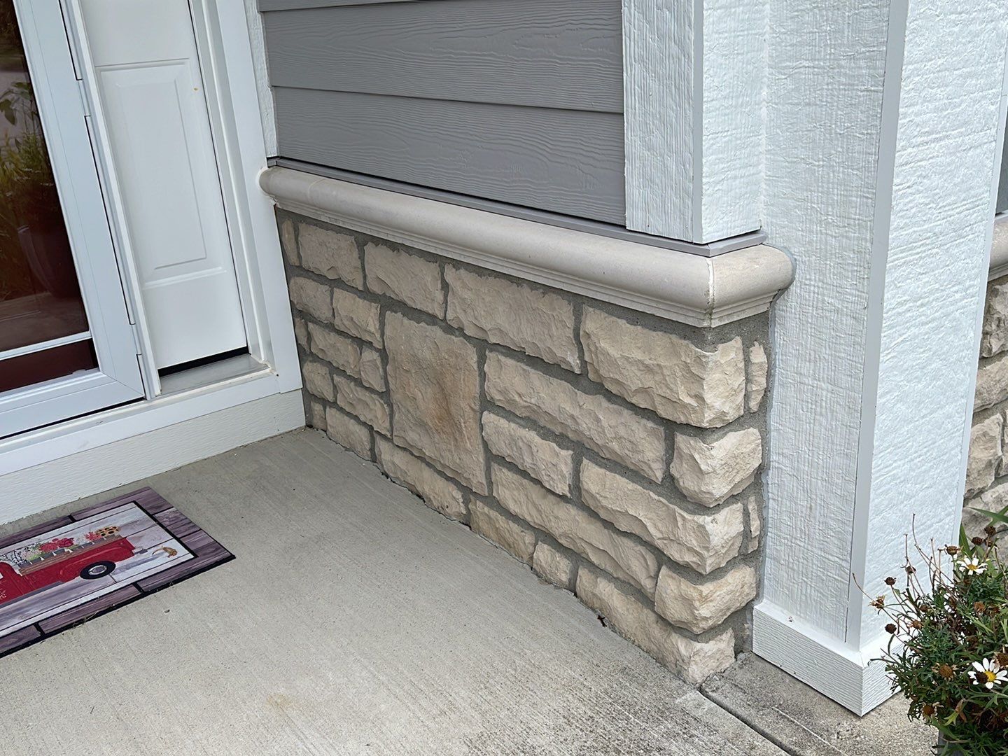Stone veneer half wall beside a front door and concrete porch