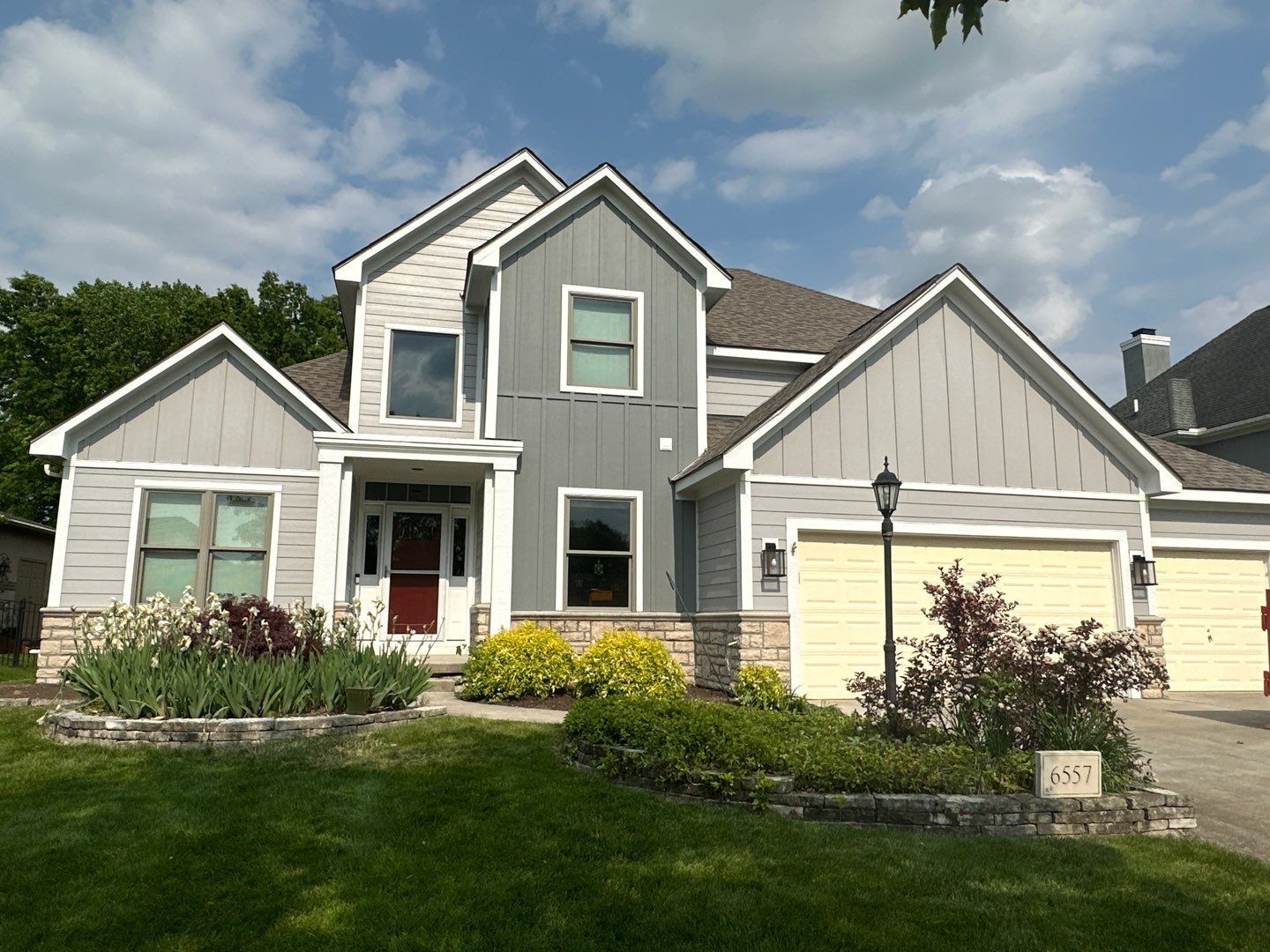 Suburban gray house with white trim, garage, and landscaped front yard under a partly cloudy sky