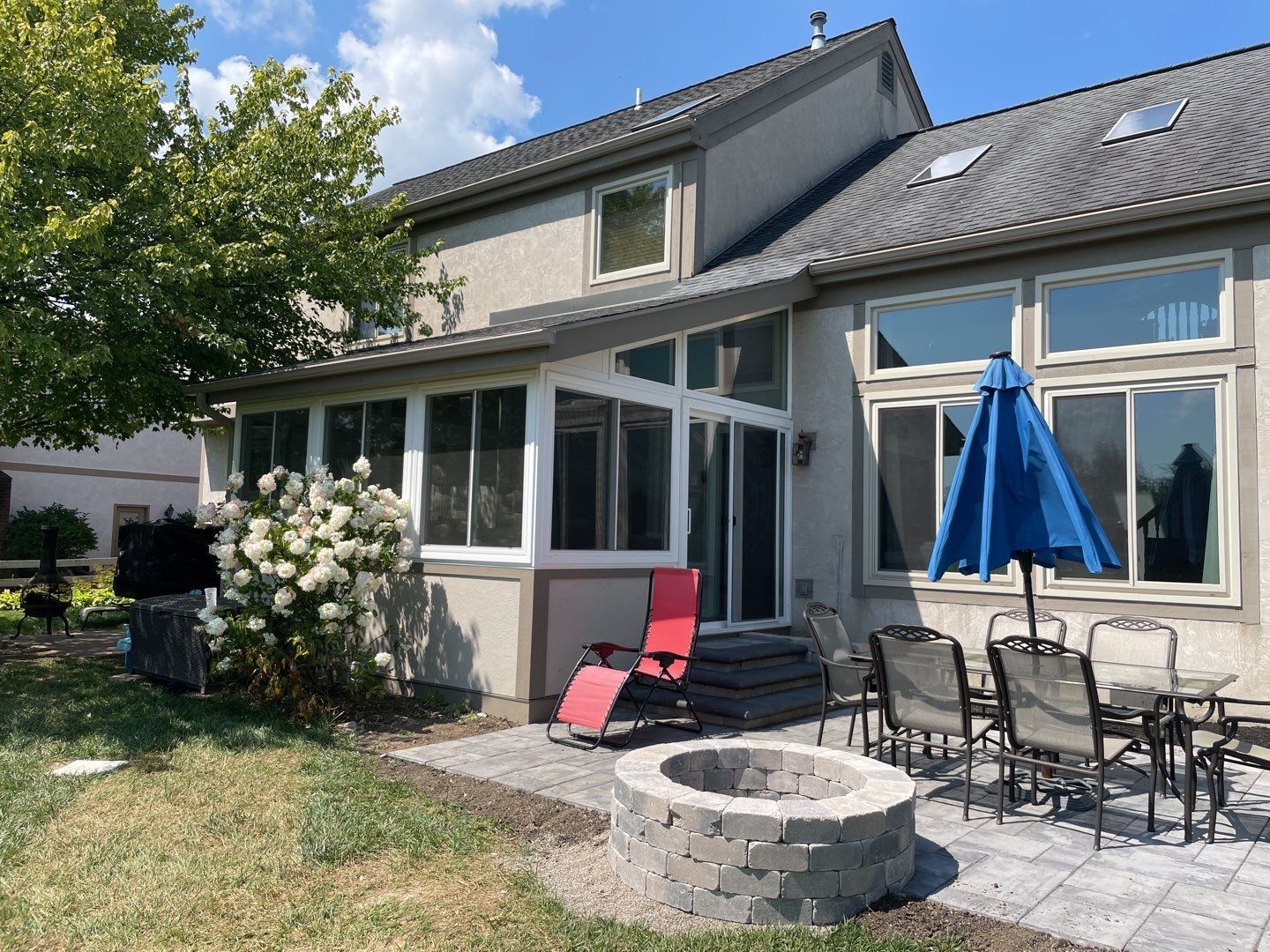 Patio with outdoor seating, blue umbrella, and stone fire pit beside a house